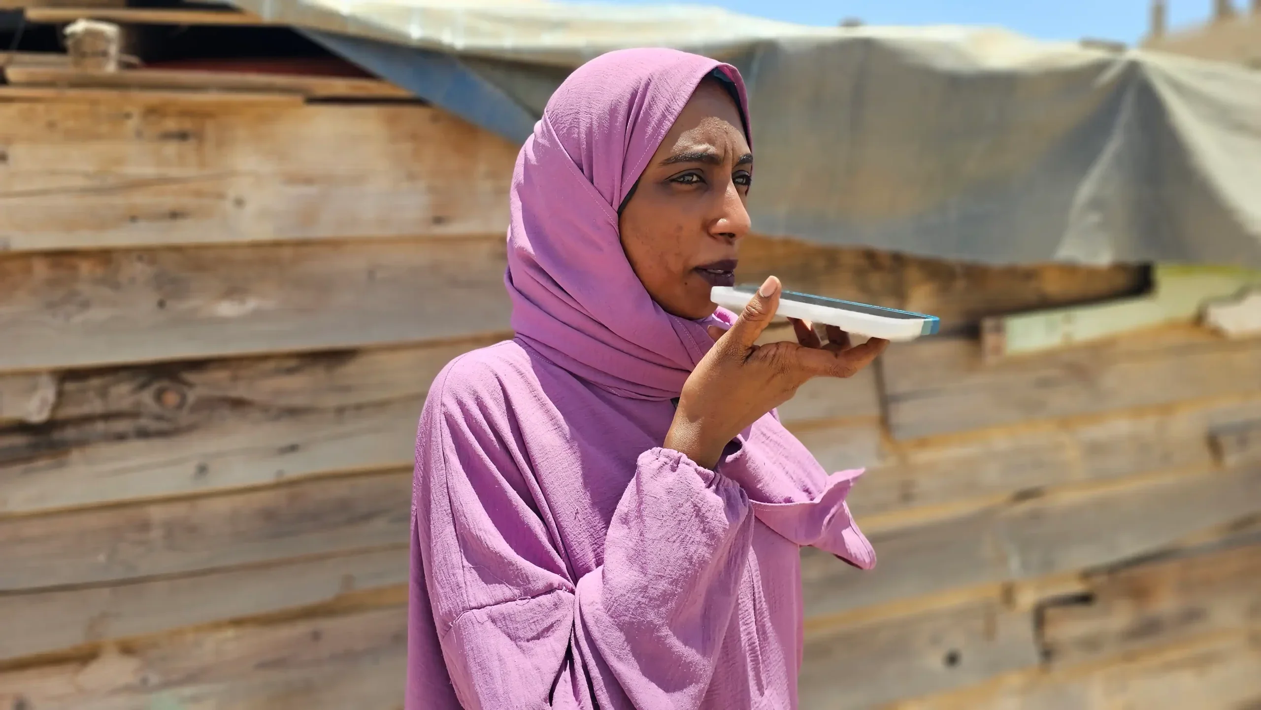 A humanitarian worker from Sudan in a pink head scarf speaks into her phone.