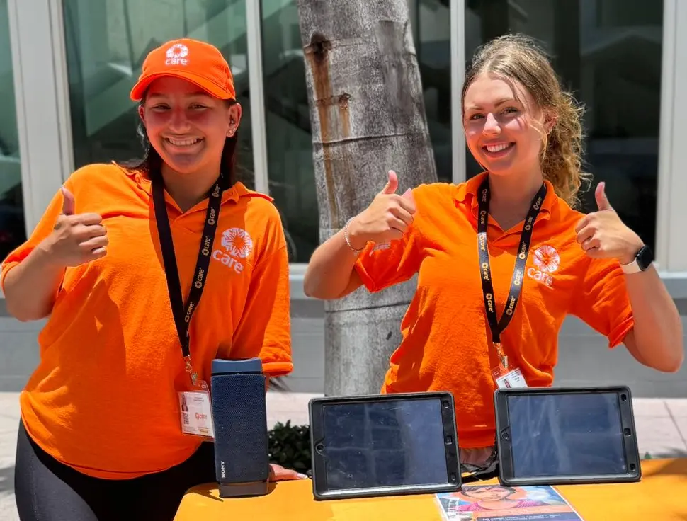 Two CARE canvassers wearing bright orange t-shirts and giving thumbs up to the camera.