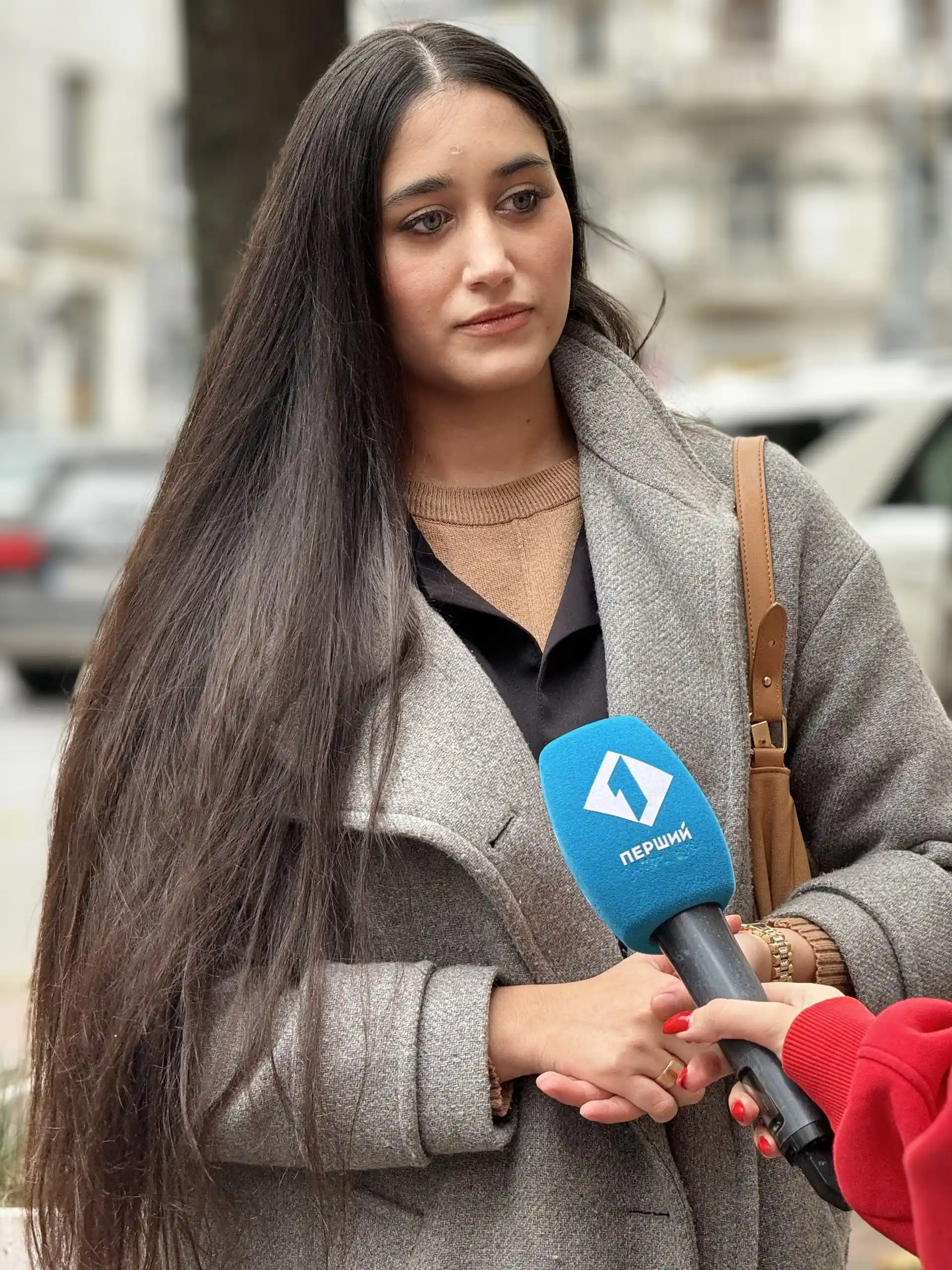 Portrait-style photo of a Roma woman speaking into a news microphone.