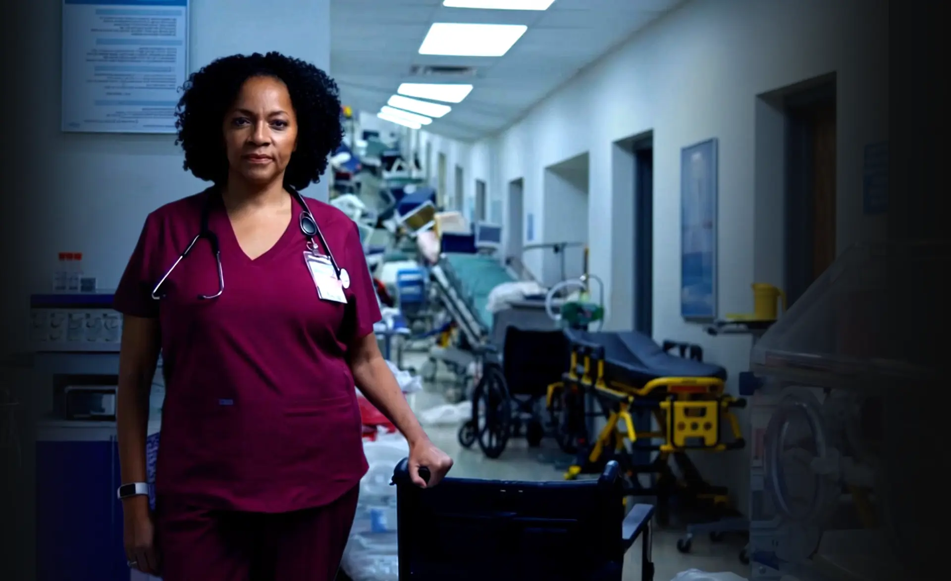 A nurse stands in front of a hospital hallway filled with clutter and broken medical equipment.