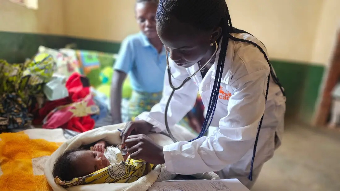 A CARE healthcare worker uses a stethoscope to examine a baby.