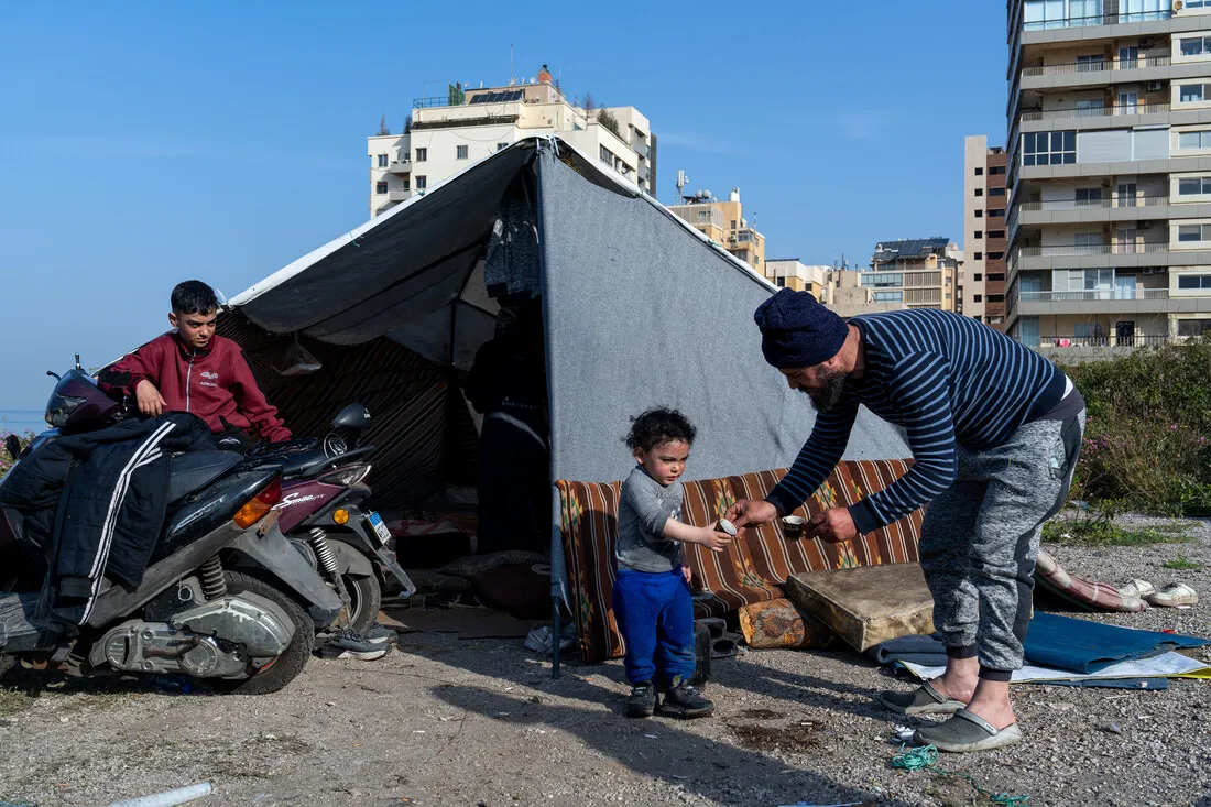 A man and child stand outside a makeshift tent, framed by urban buildings. A boy sits on a scooter nearby, conveying resilience and adaptability.