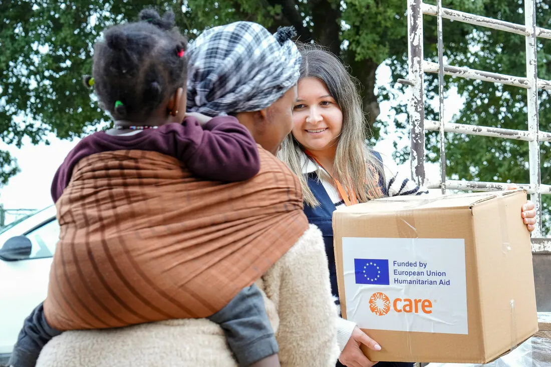 A smiling aid worker hands a box labeled 