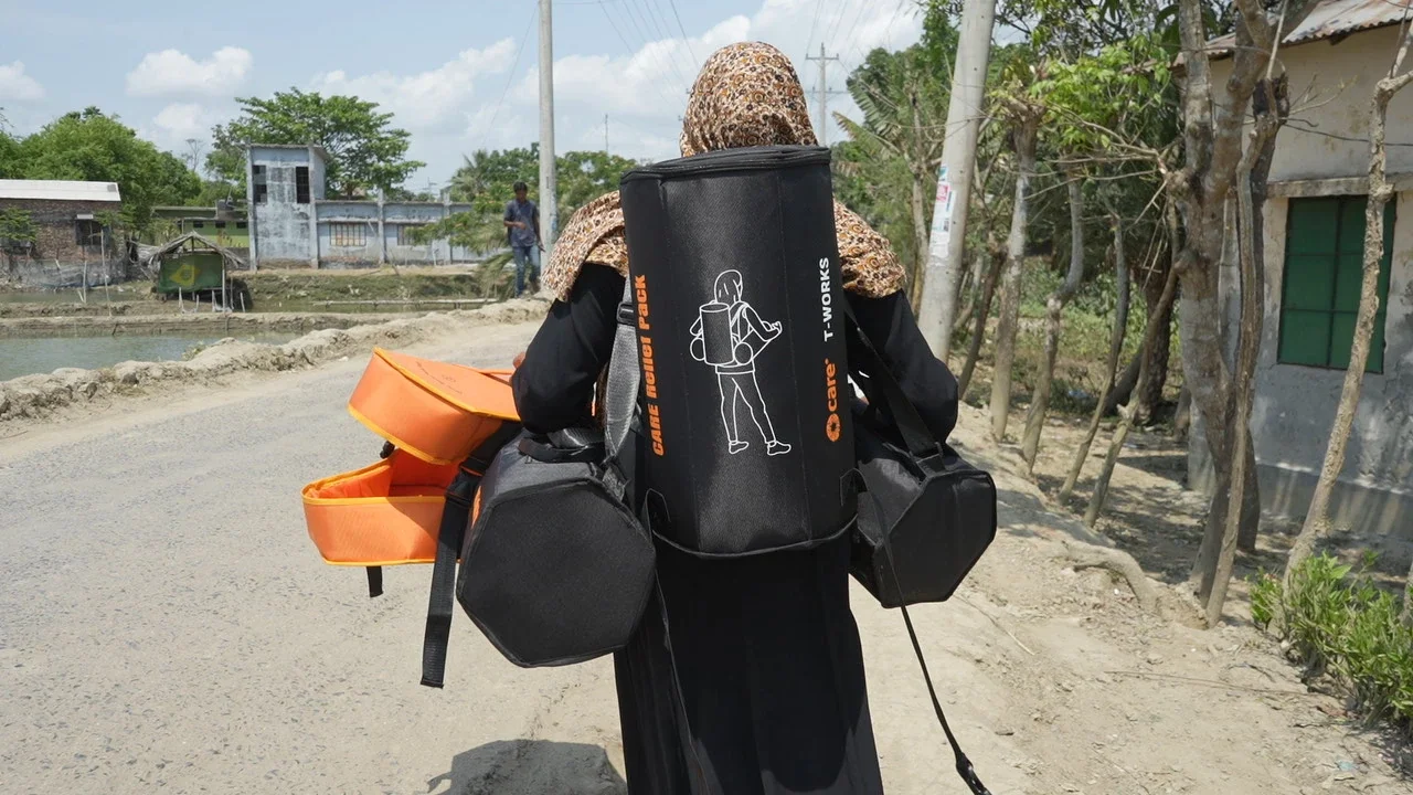 Woman carrying multiple CARE PACKAGE® for Emergencies packs down a rural road.