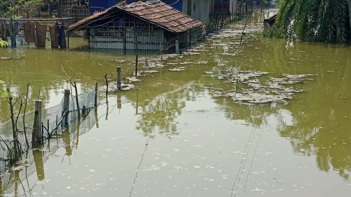 A flooded rural village in Bangladesh with a house partially submerged in murky green water.