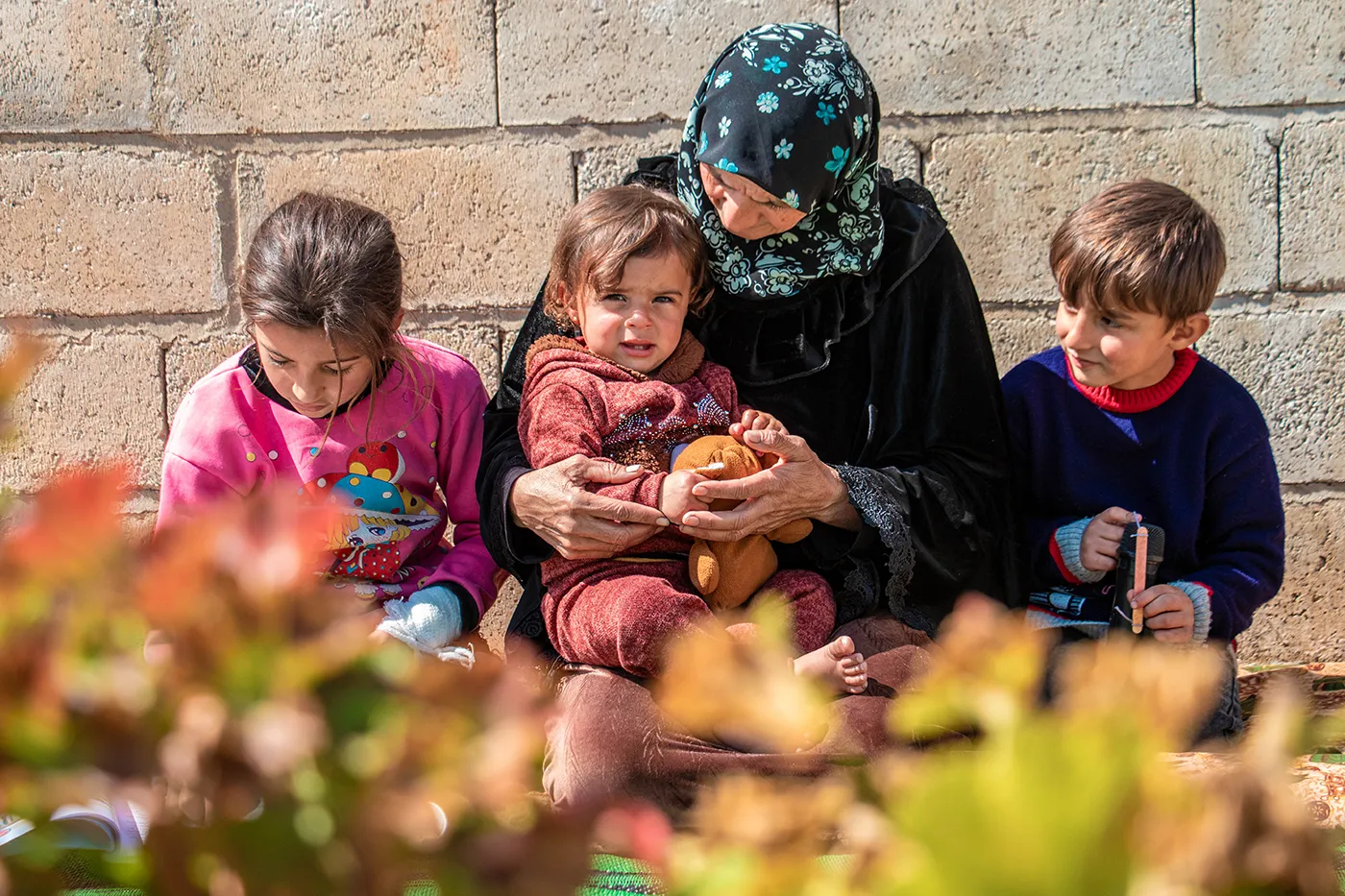 A Syrian woman comforts a small child in her arms, while two children sit on either side of her.