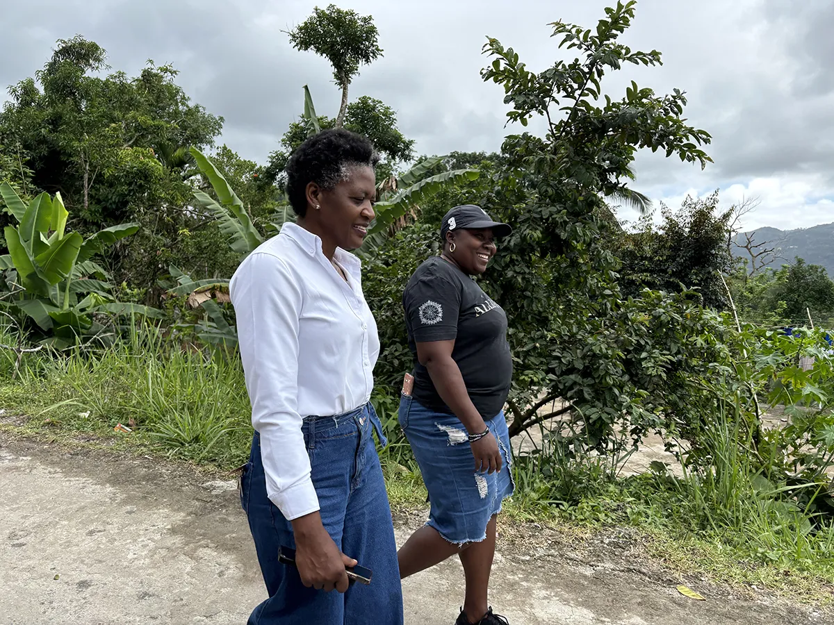 Two Jamaican women walk side by side down a sandy path.