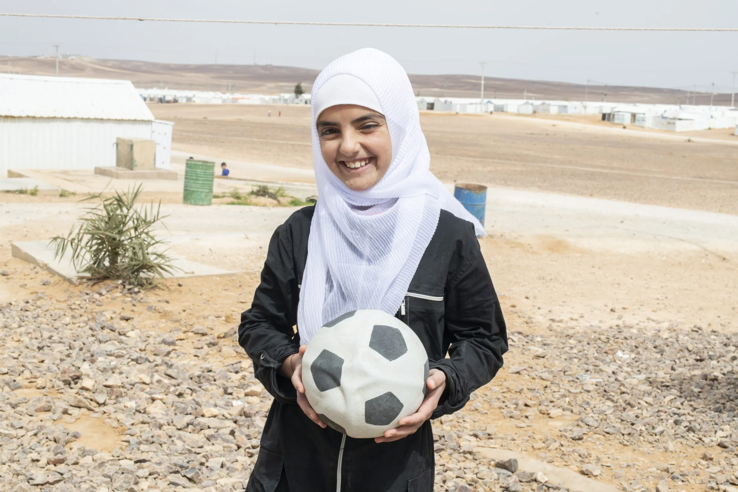 A young Syrian teenager in a headscarf holds a soccer ball at Azraq refugee camp in Jordan.
