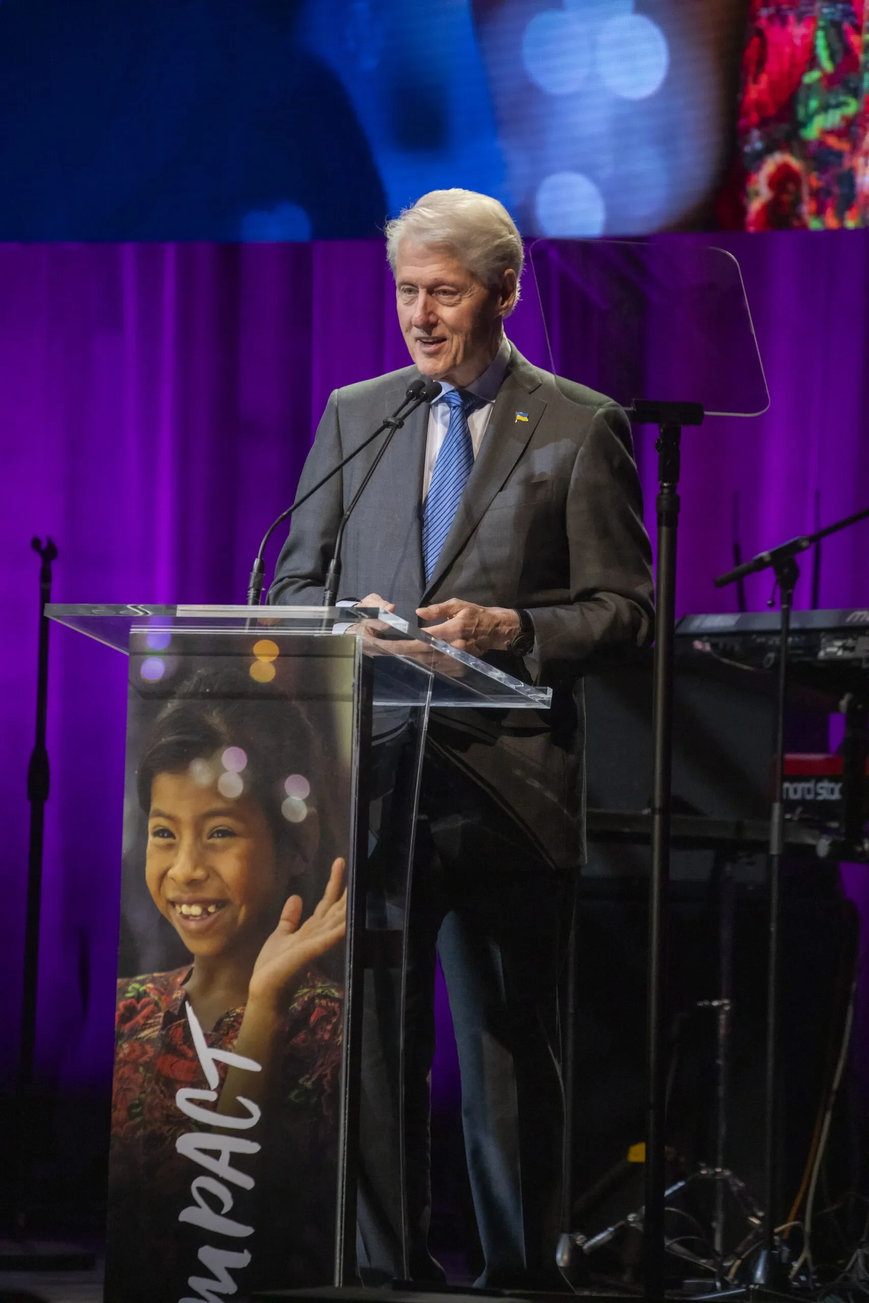 President Bill Clinton standing at a podium, speaking at CARE’s Impact Awards show.