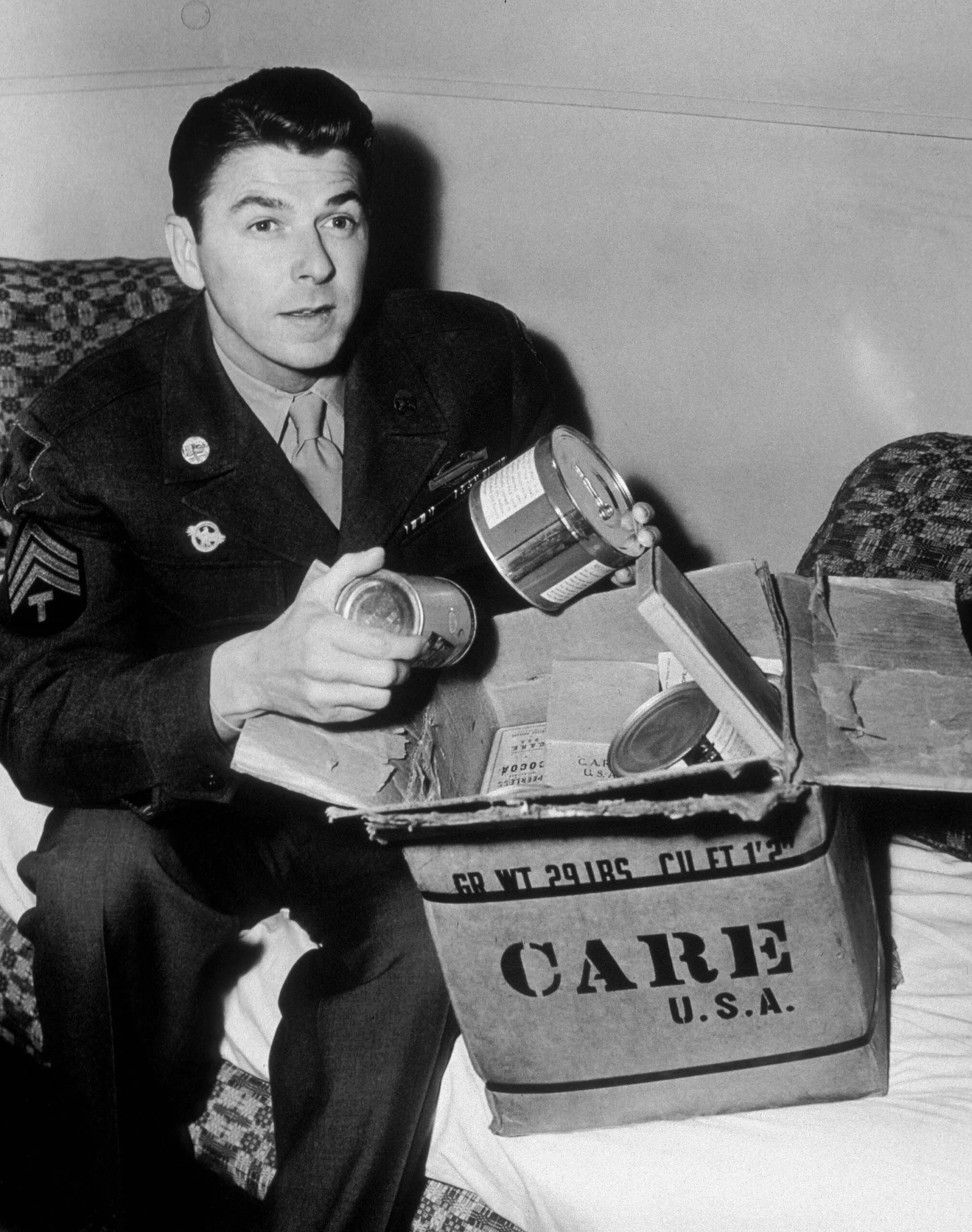 President Ronal Reagan sitting next to a CARE PACKAGE dressed in a military uniform.