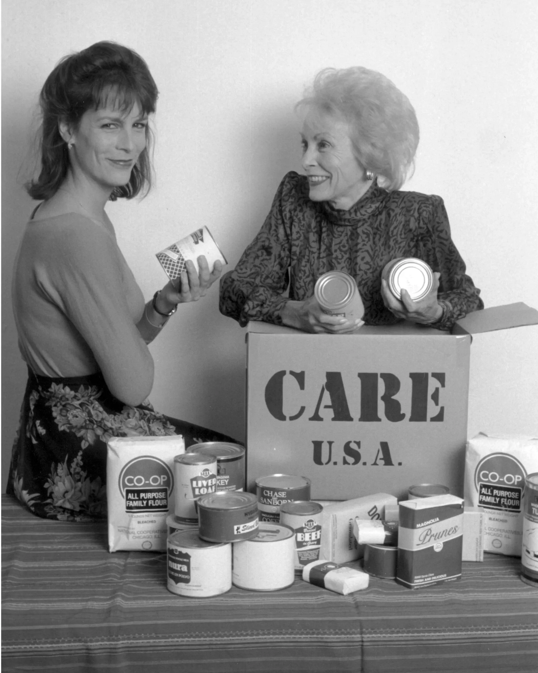 Actress Janet Leigh and her daughter Jamie Lee Curtis pose by a CARE PACKAGE with food items in their hands.