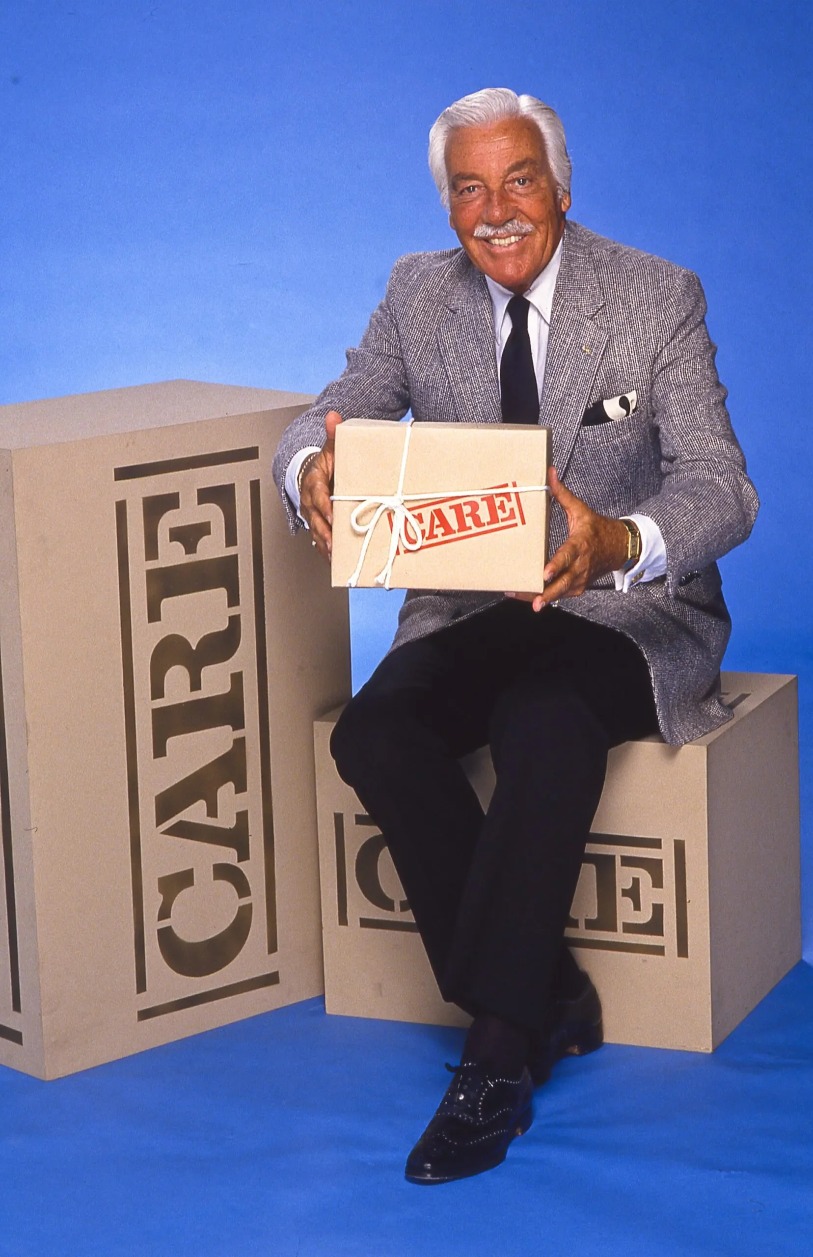 Actor Cesar Romero poses with a CARE PACKAGE for a television special promo.