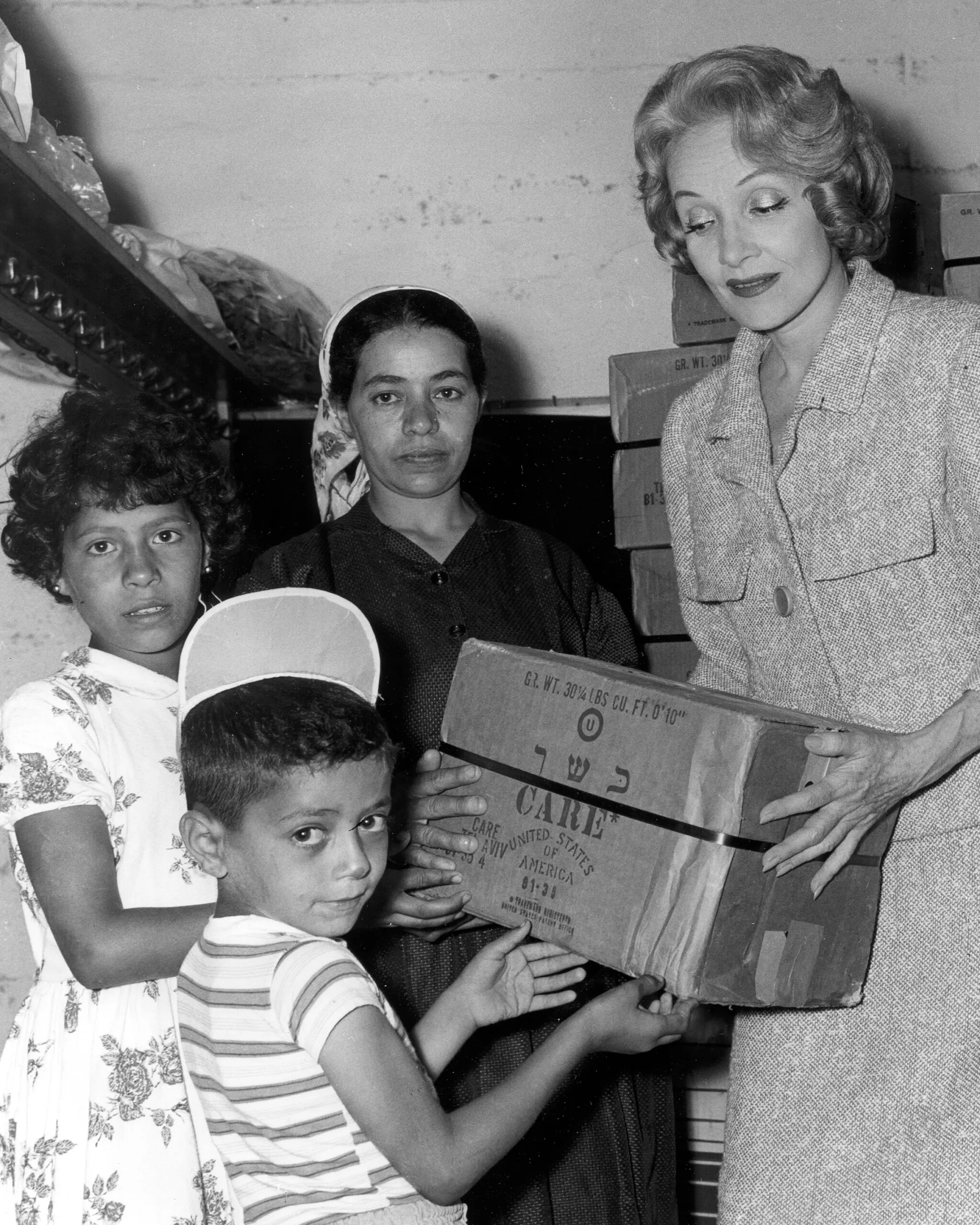 Actress Marlene Dietrich hands a CARE PACKAGE box to children.