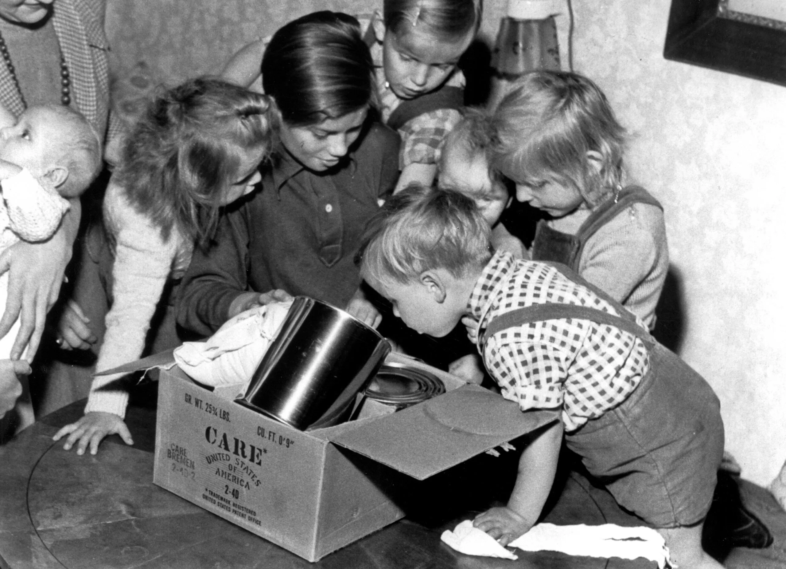 A black and white photo of a group of children looking inside a CARE PACKAGE box.