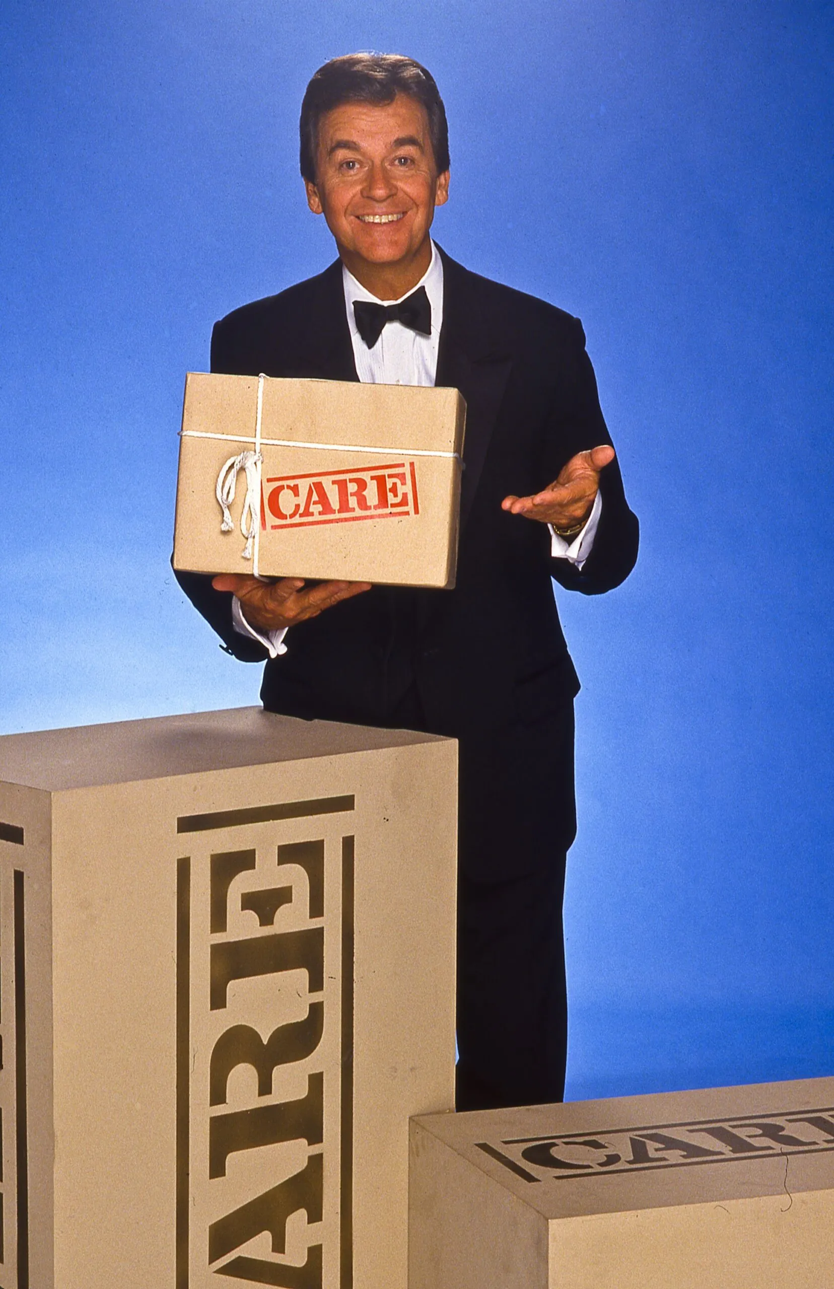 Dick Clark poses with a CARE PACKAGE for a television special promo.