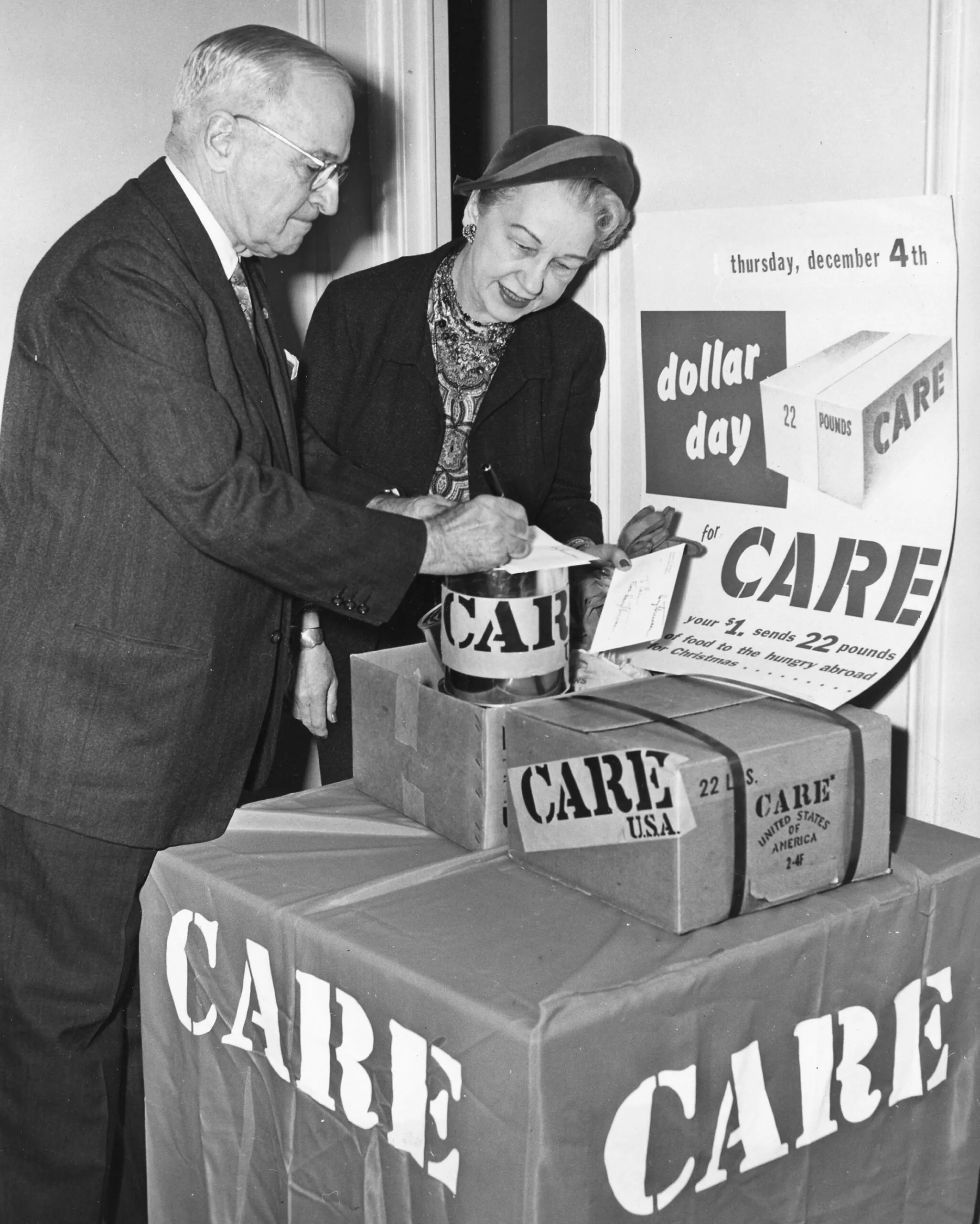 A historical image of President Harry S. Truman signing a donation on top of a CARE box.