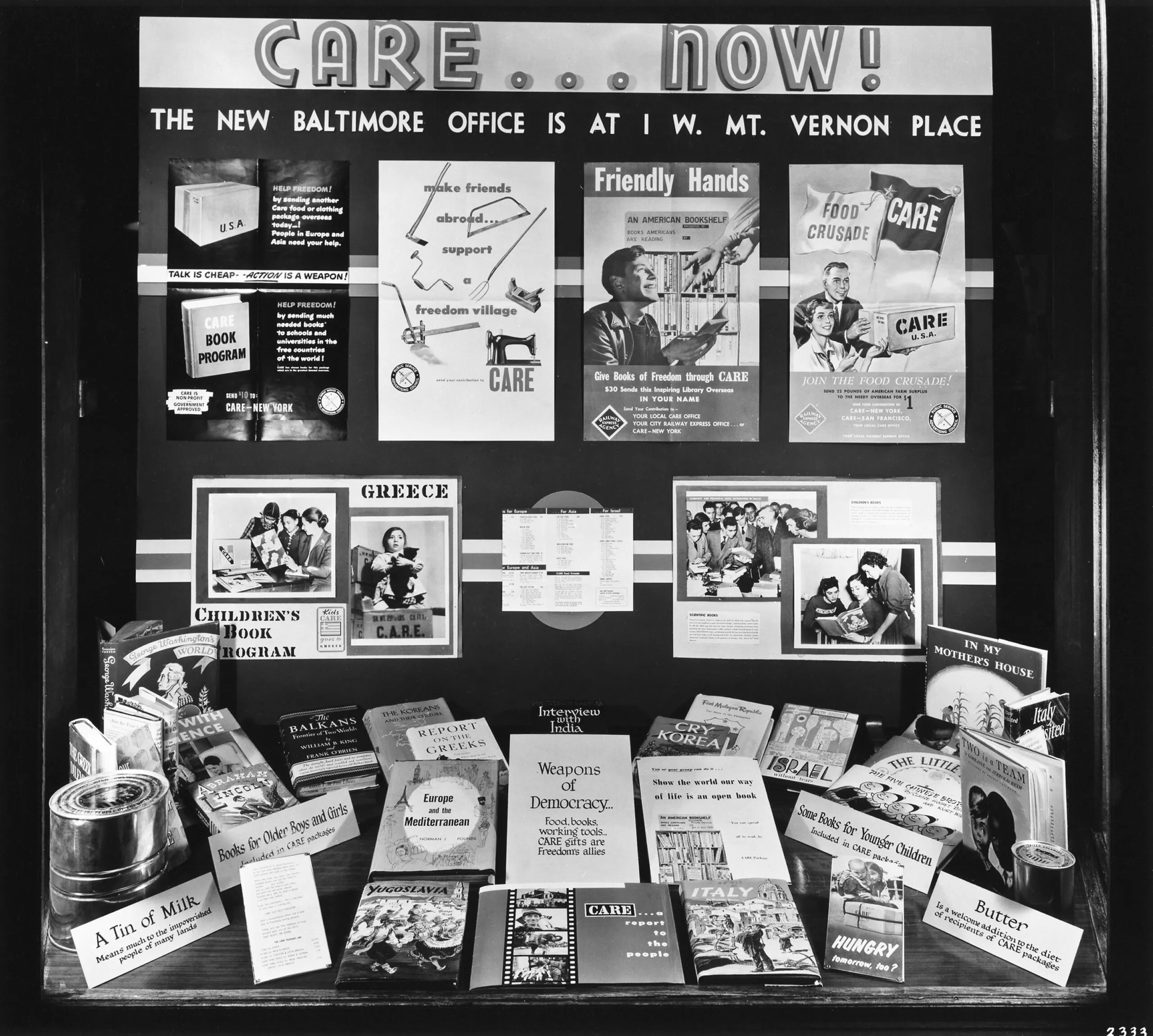 A black and white photo of a CARE ad display that has posters and items from various CARE programs.