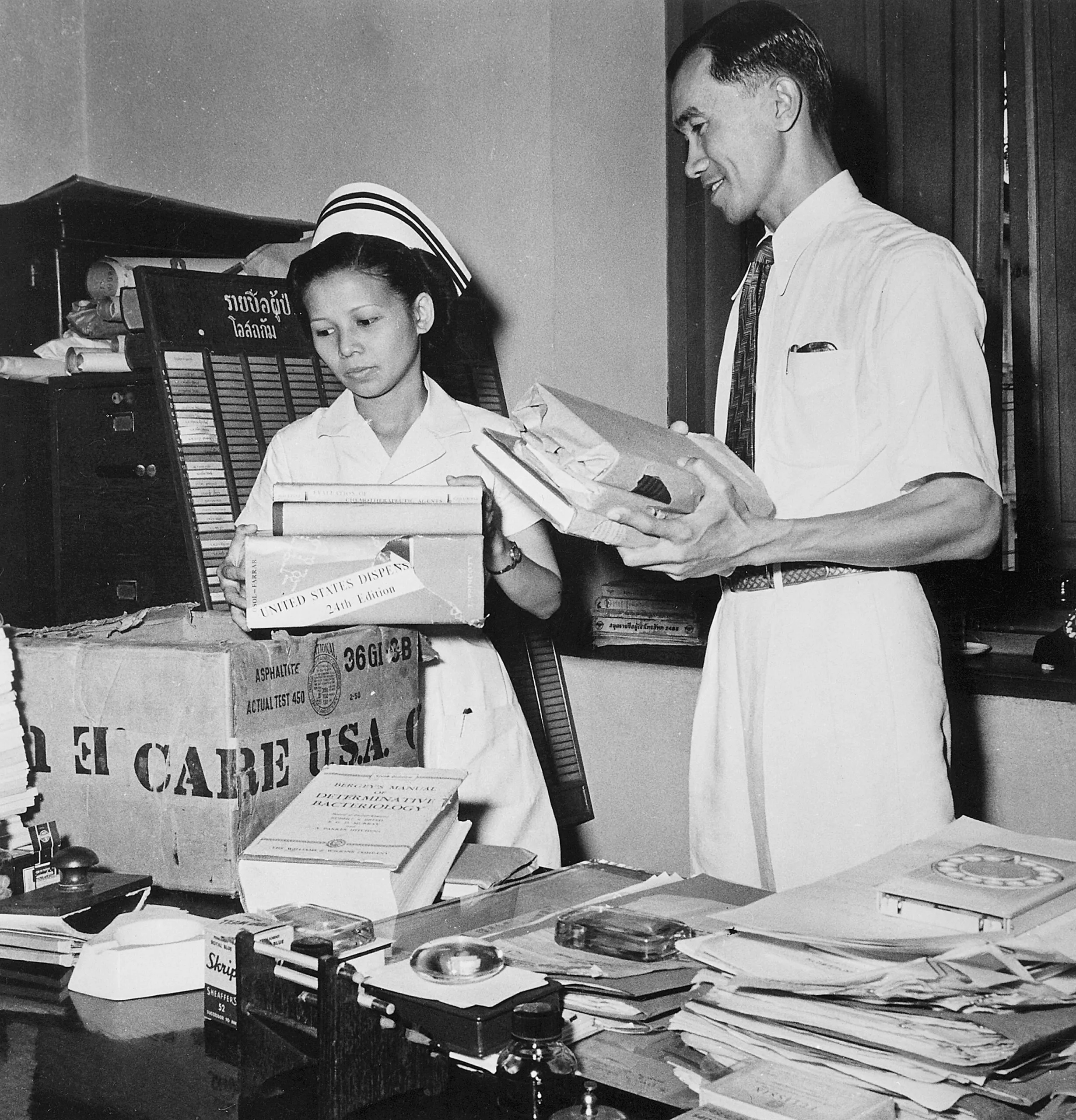 A black and white photo of a doctor and nurse opening a CARE PACKAGE filled with medical books.