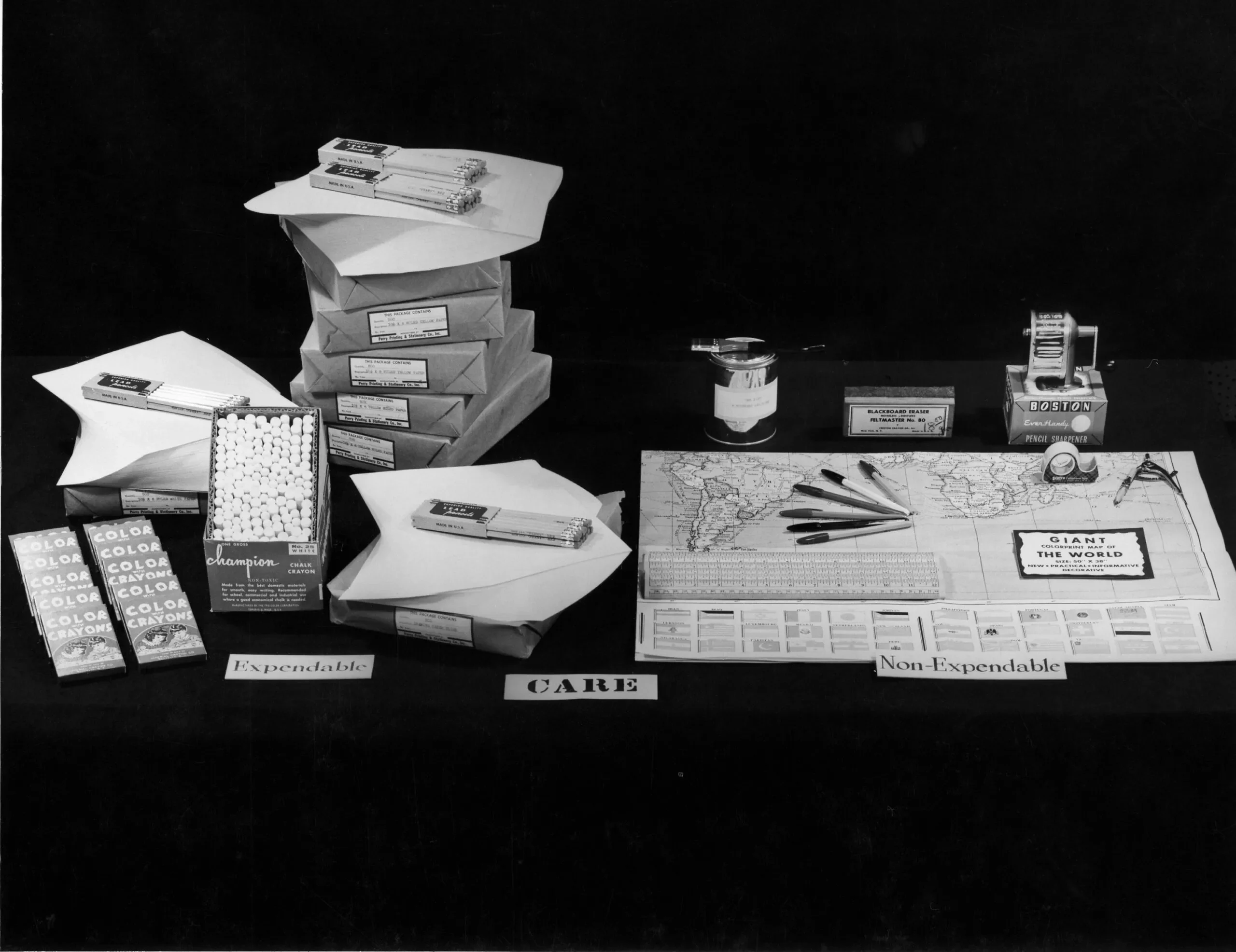 A historical image of items laid out from a CARE PACKAGE Self-Help Schoolroom Kit. The kit includes a map, pencils, chalk, erasers, pens, rulers and more.