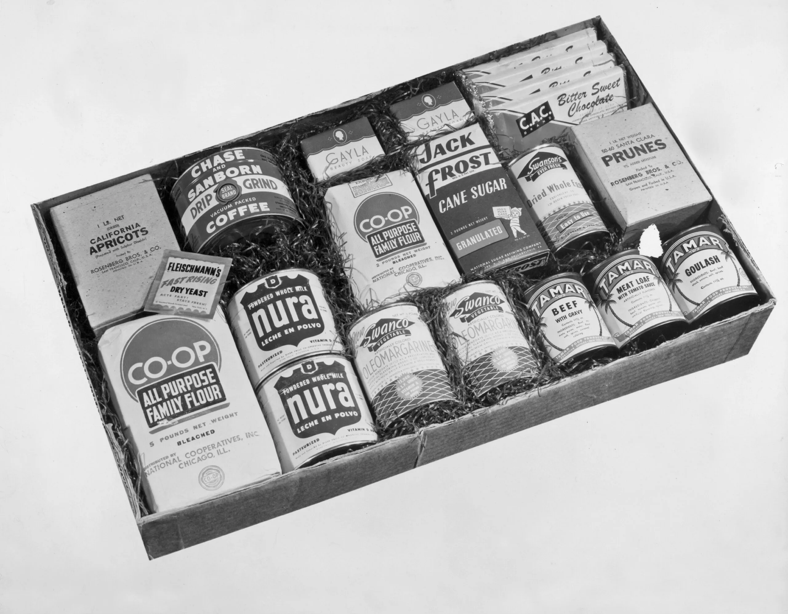 A historical image of an open kosher food CARE PACKAGE. The items inside the box include: luncheon meat, coffee, sugar, chocolate, soup and more.