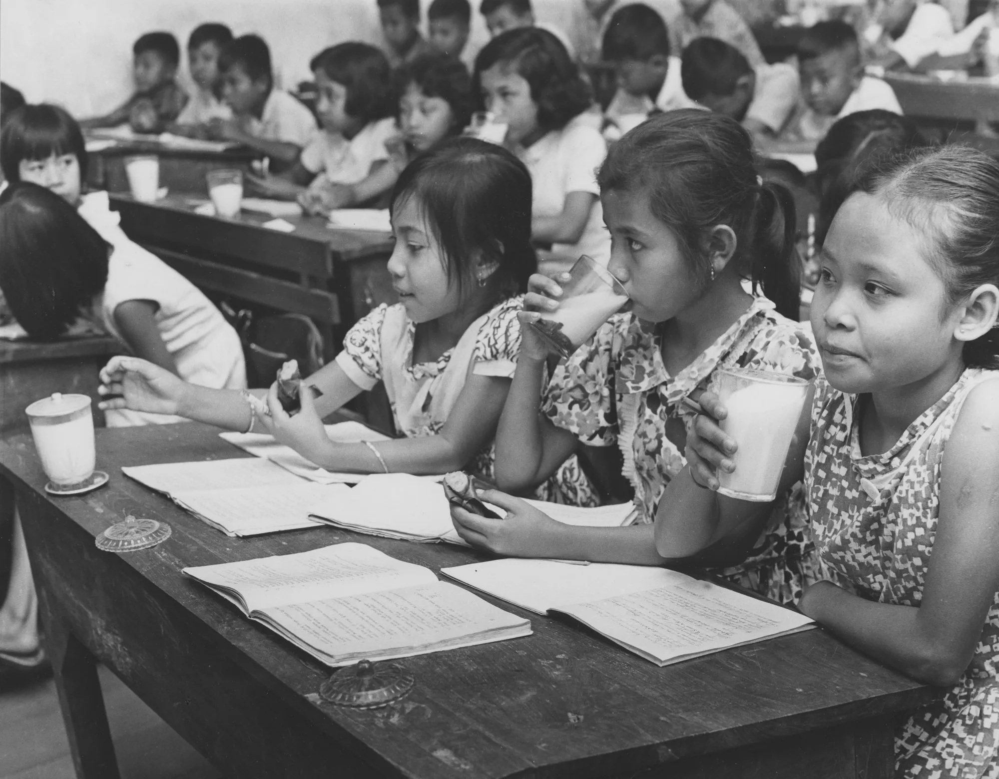 A historical image of young girls in school, sitting at tables and drinking milk.