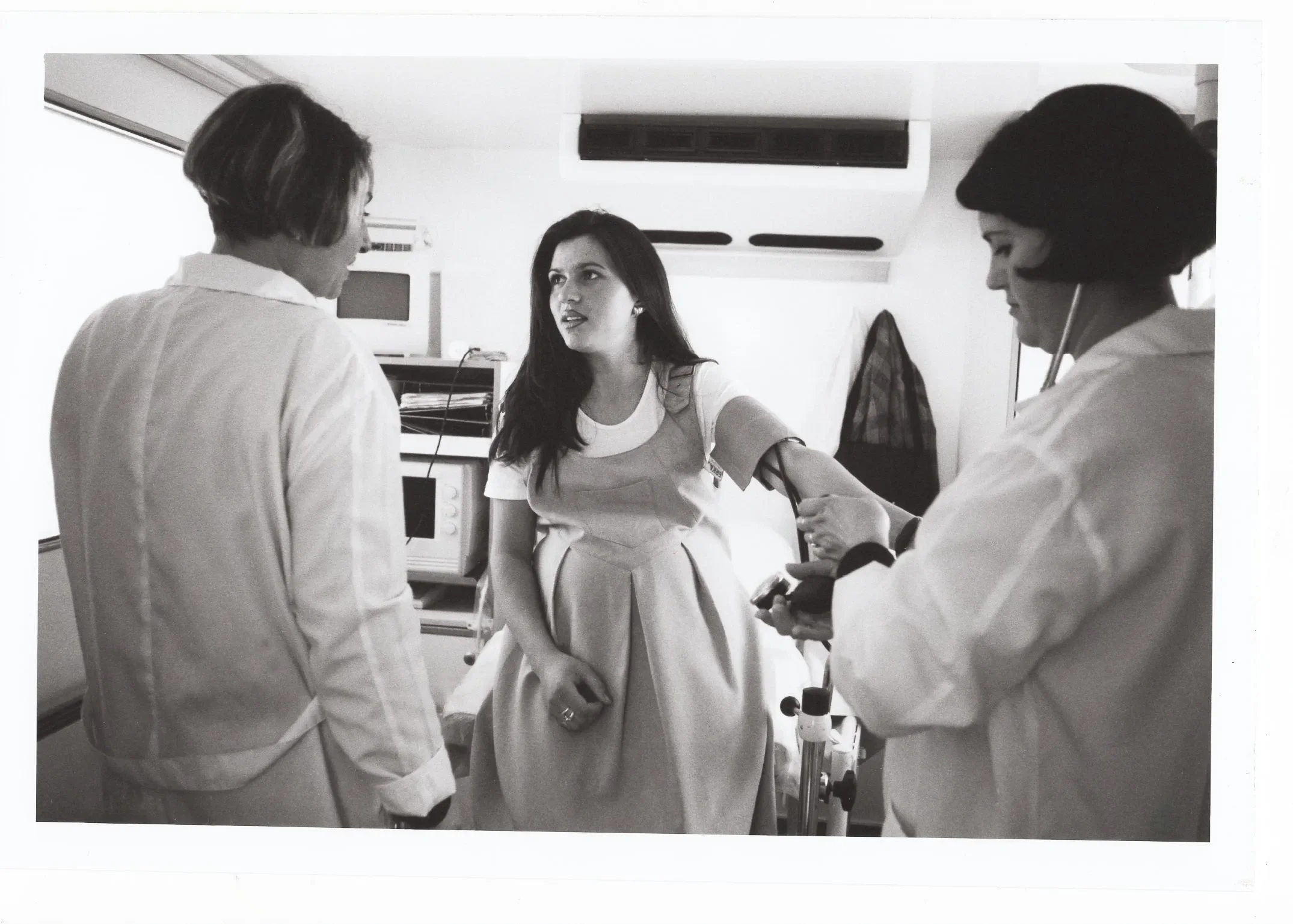 A pregnant woman is being seen by two women of the medical staff at a clinic.