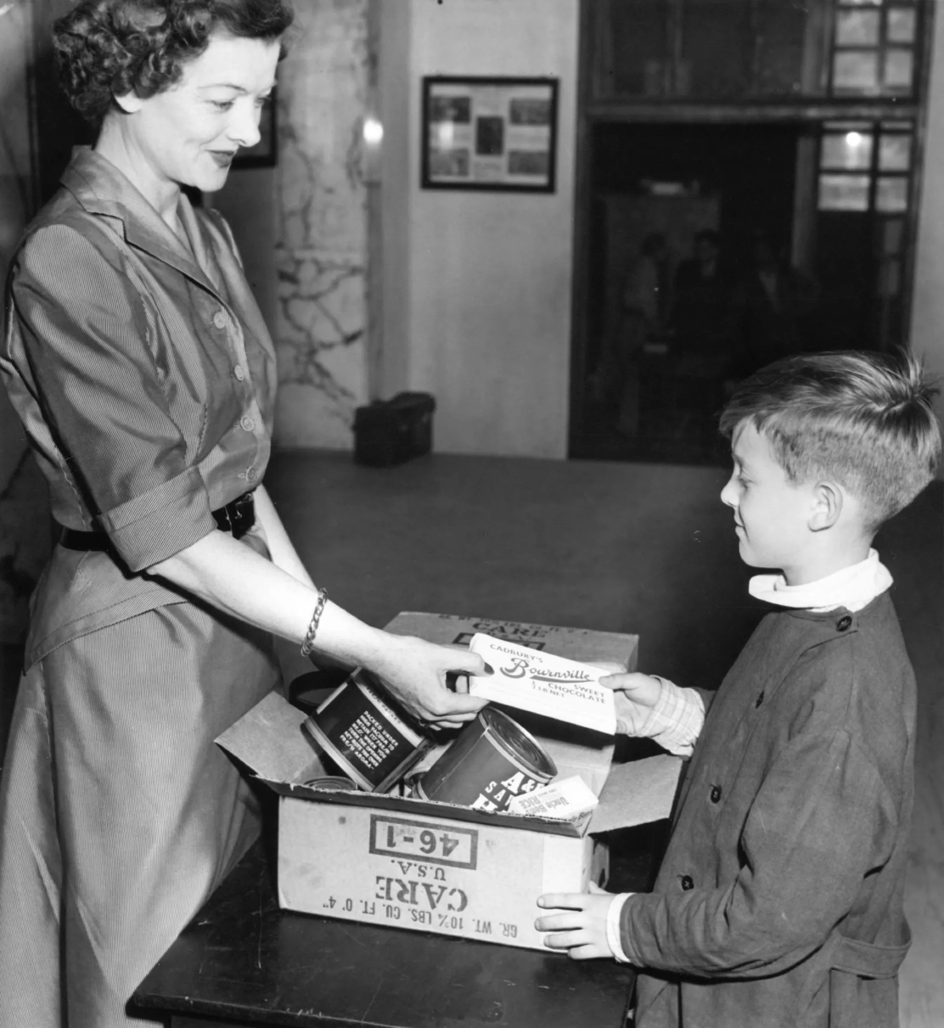 Actress Myrna Loy showing a young child a CARE PACKAGE.