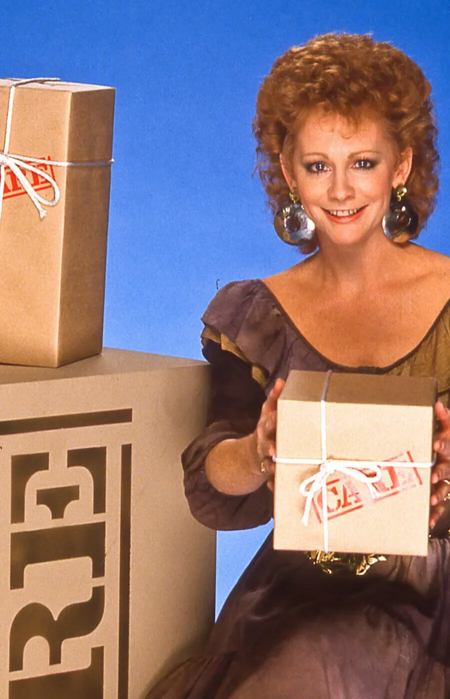 Country music star Reba McEntire poses next to a stack of CARE PACKAGE boxes for a television special promo.