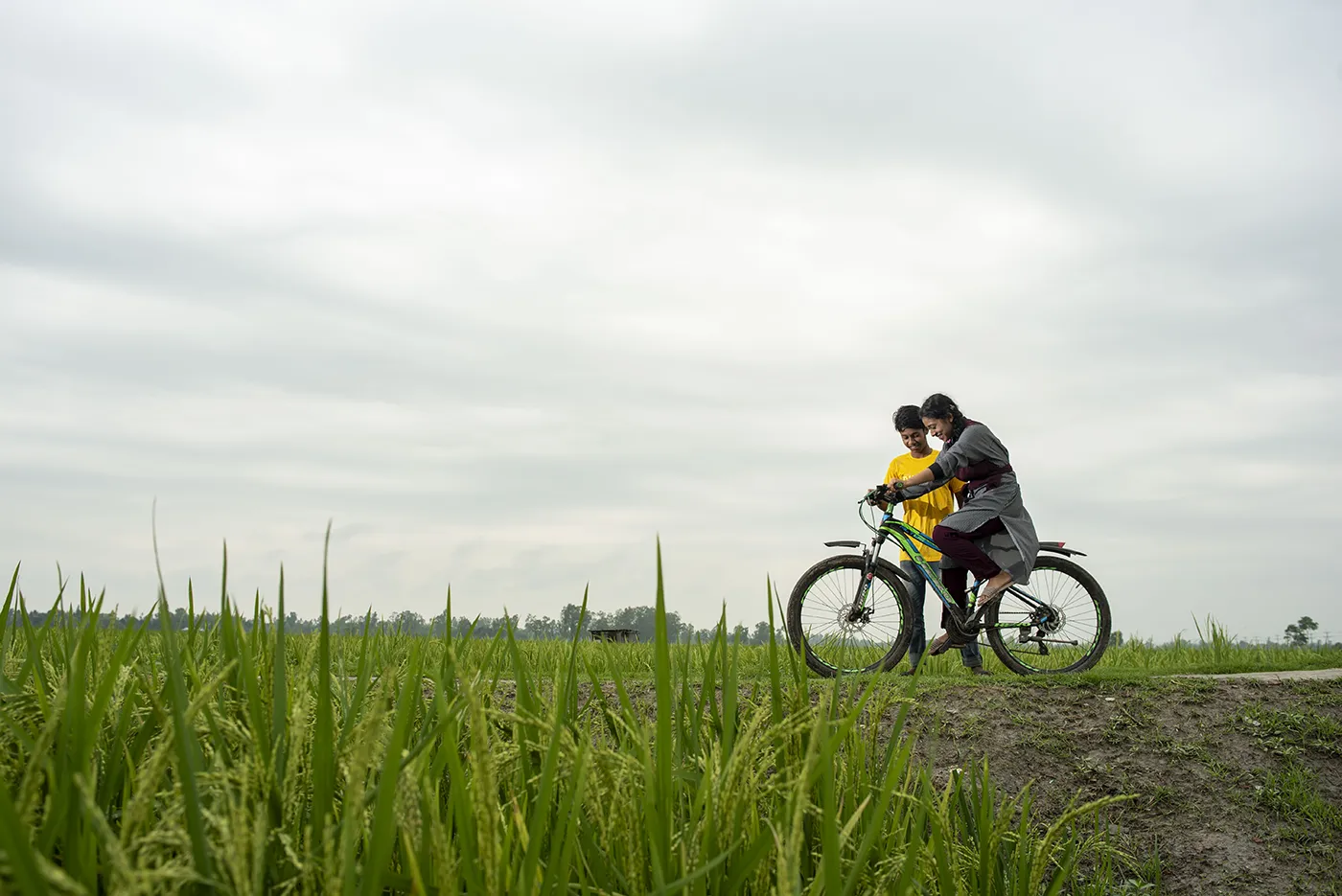 Two people ride a bike through a field.