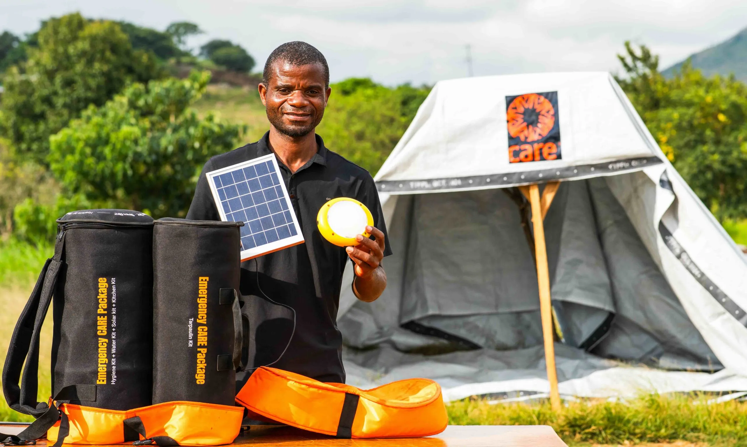 Samuel Zonda demonstrates a solar charger and emergency light included in a CARE PACKAGE for Emergencies in Malawi. A temporary shelter made from a CARE tarp is in the background.