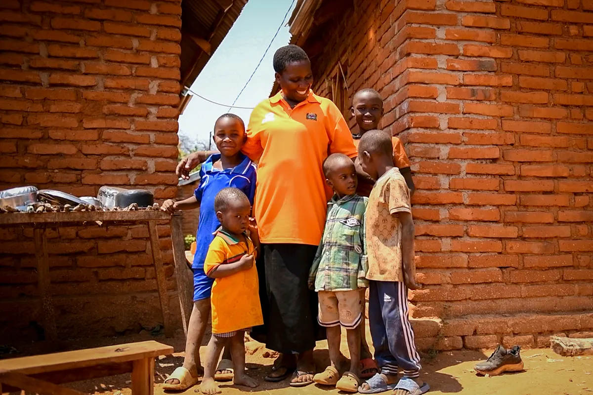 A woman wearing a bright orange shirt smiles at her five children.