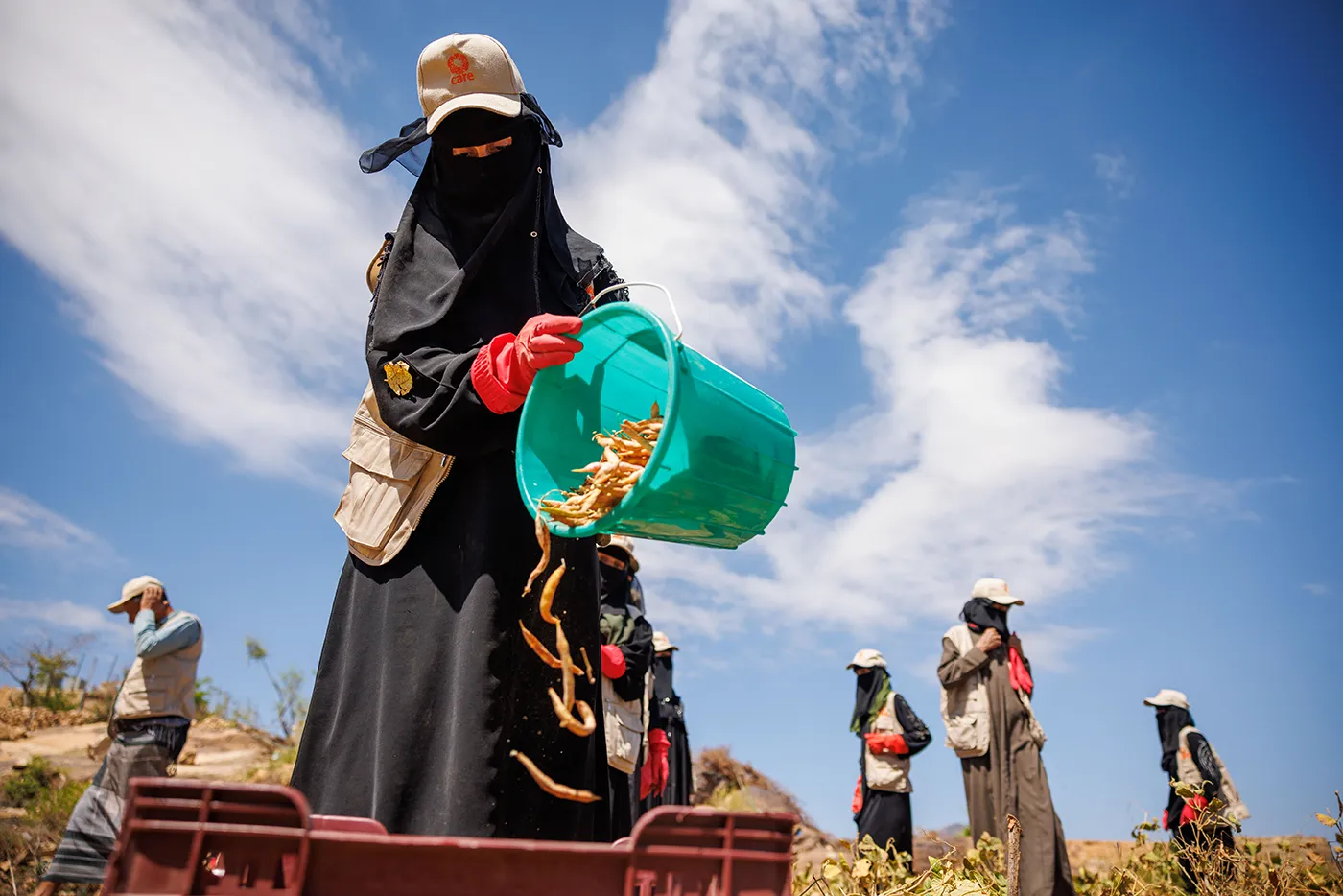 A Yemeni woman pours beans from a bucket into a larger tub.