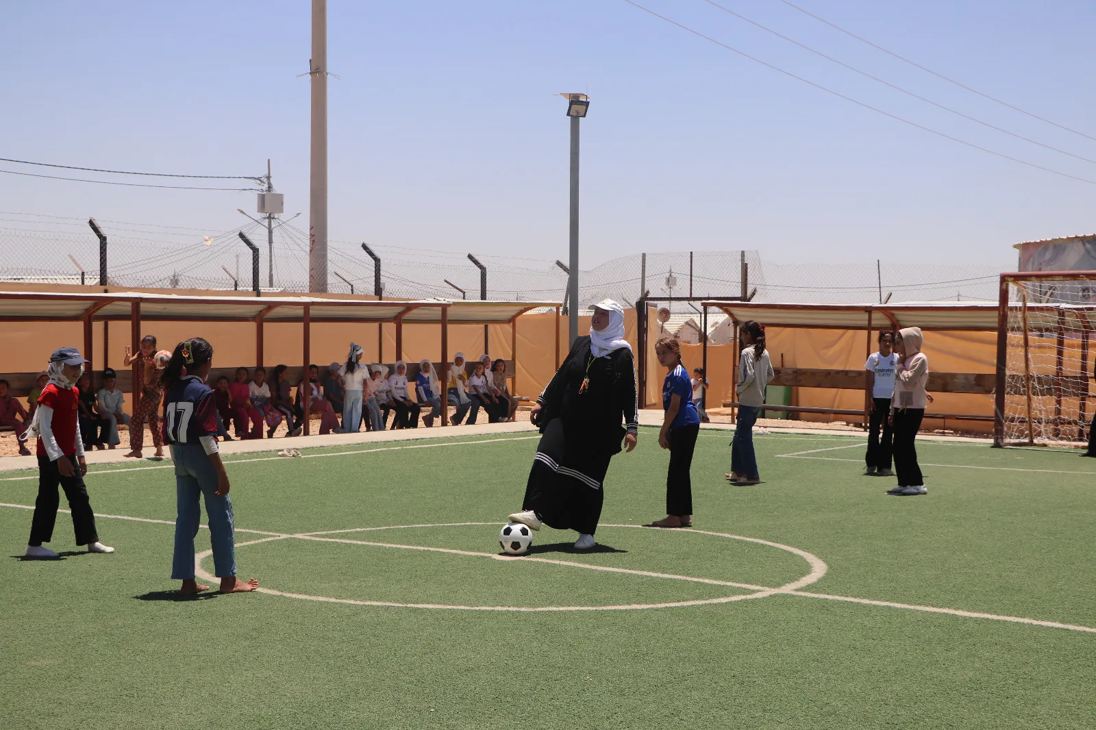 A woman standing in the middle of a soccer field with players around her.
