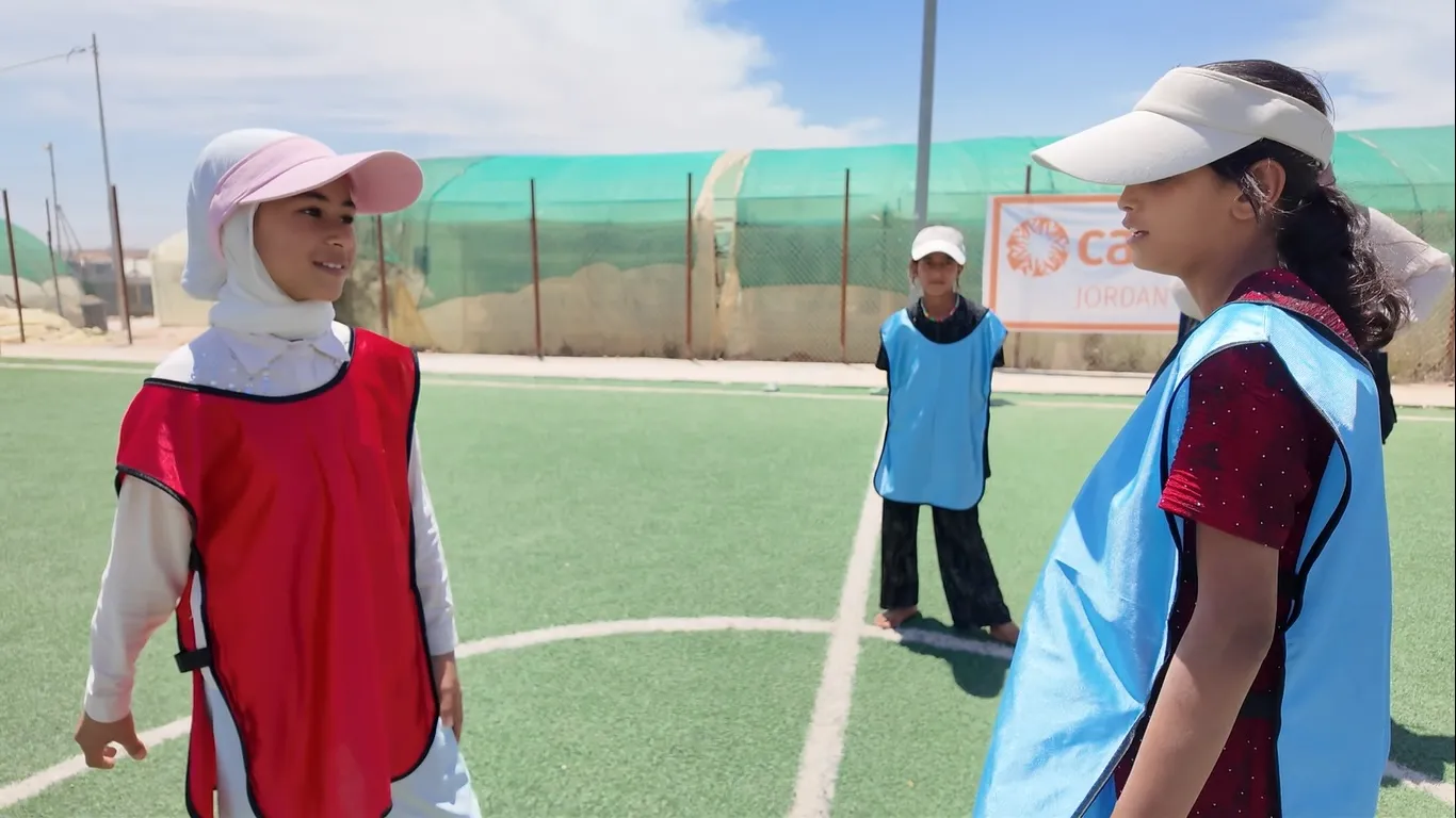 Two young girls stand looking at each other on a soccer field.
