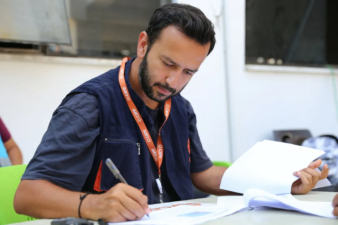 A man wearing a CARE badge writes down notes in a report.
