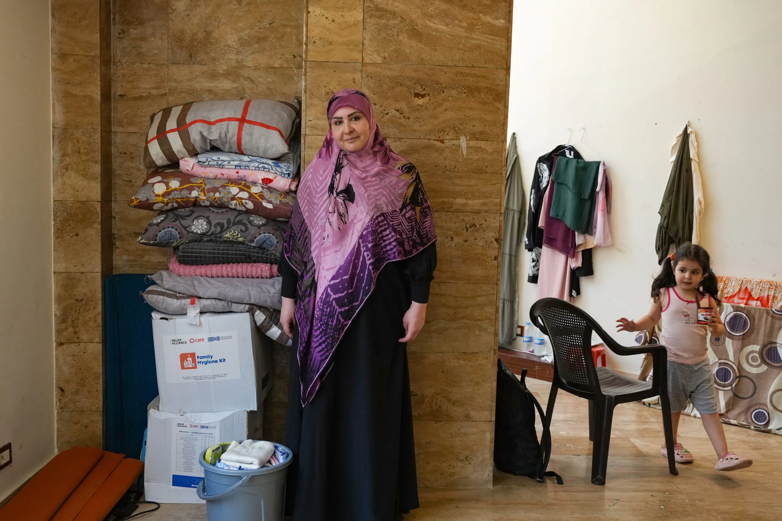 A woman stands next to a box of supplies, towels and blankets with her daughter in the background.