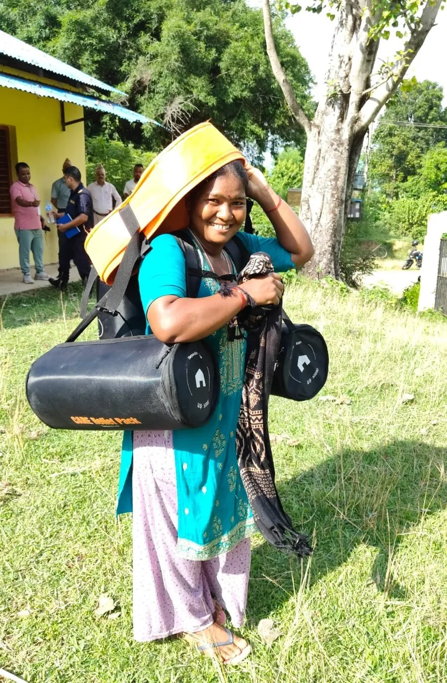 Smiling Nepalese woman carrying CARE relief packs and resources for community recovery.