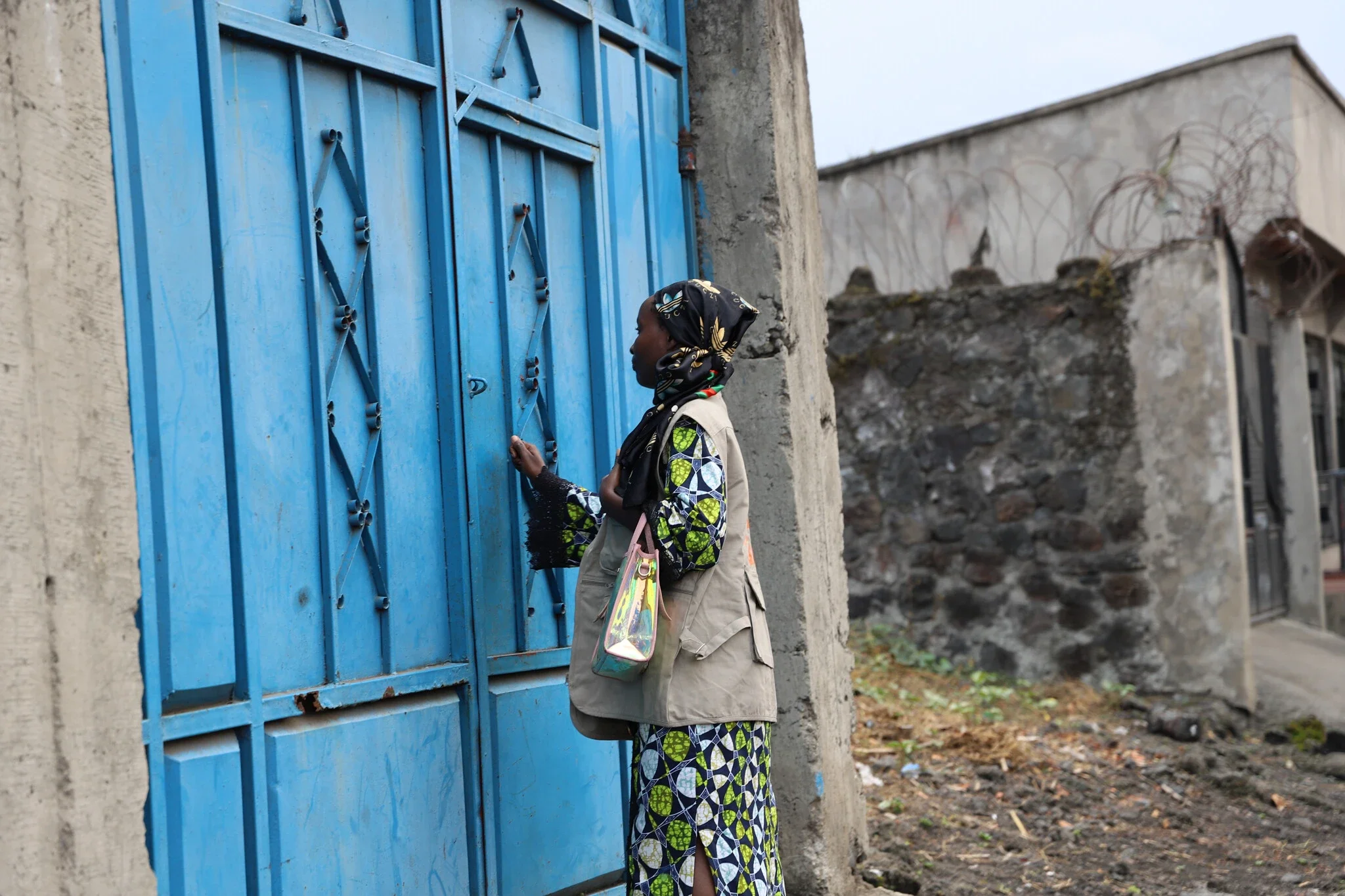 Woman standing and knocking on blue gate door.