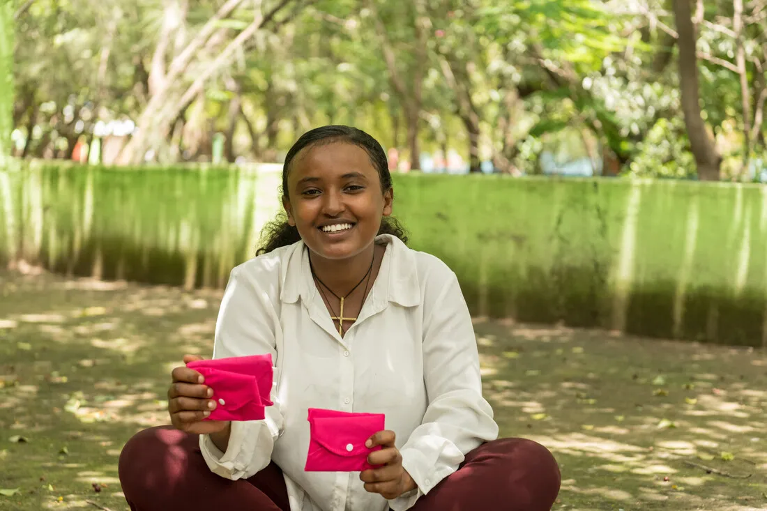 A teen girl holds up menstruation pads in hot pink cloth wrapping.
