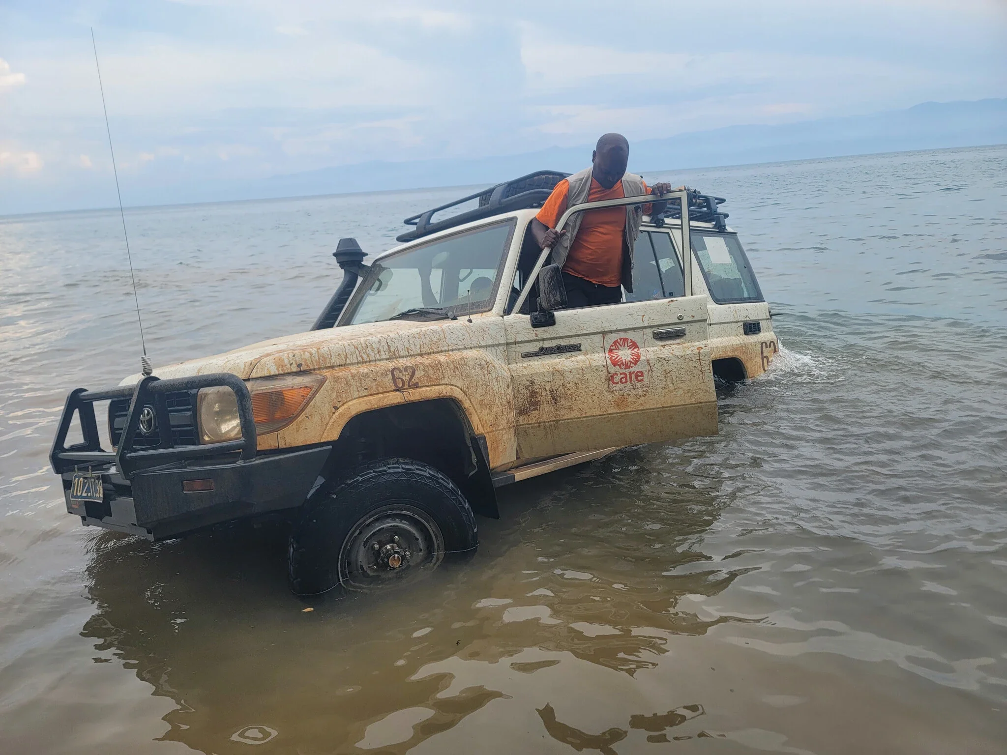 Car partially submerged in a lake with a man standing in the driver's doorway.