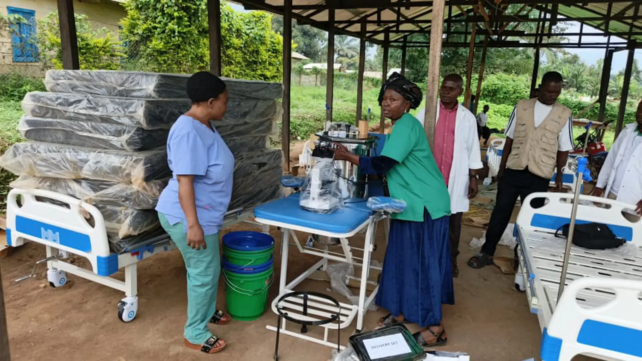 Aid workers in outdoor clinic with hospital beds.