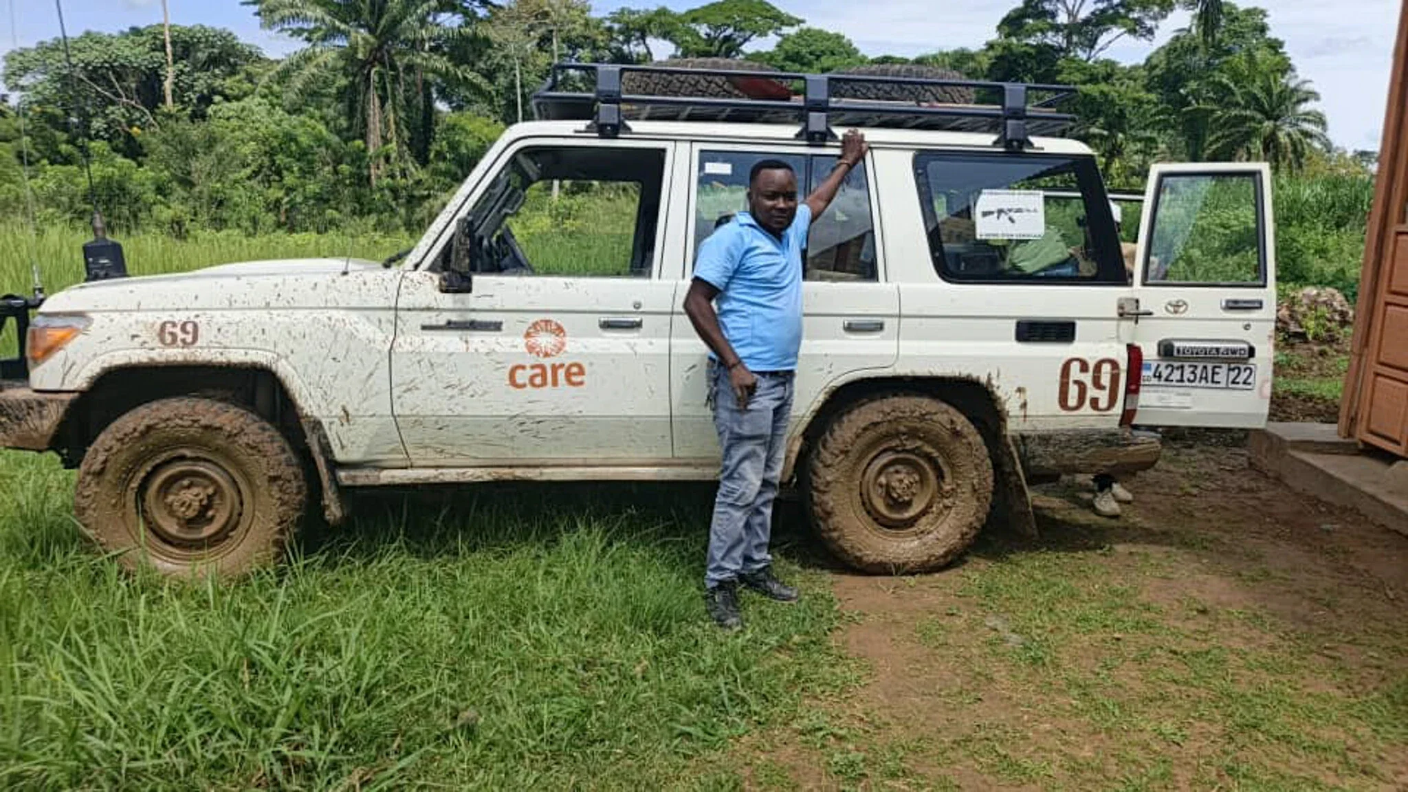 A man standing next to a truck with dirty wheels on a dirt road.