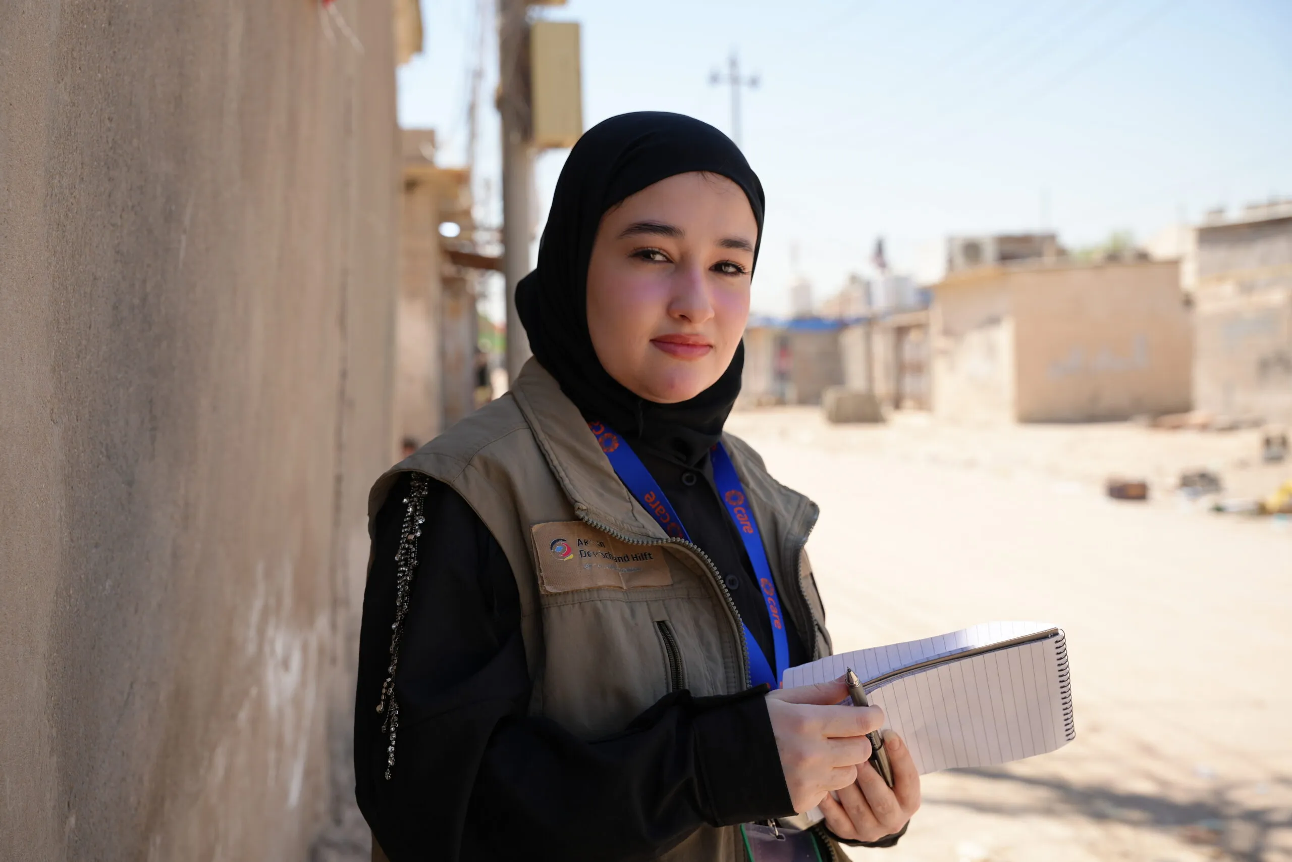 A young woman with a notepad and pen standing outside on a sunny day in Basra, Iraq.