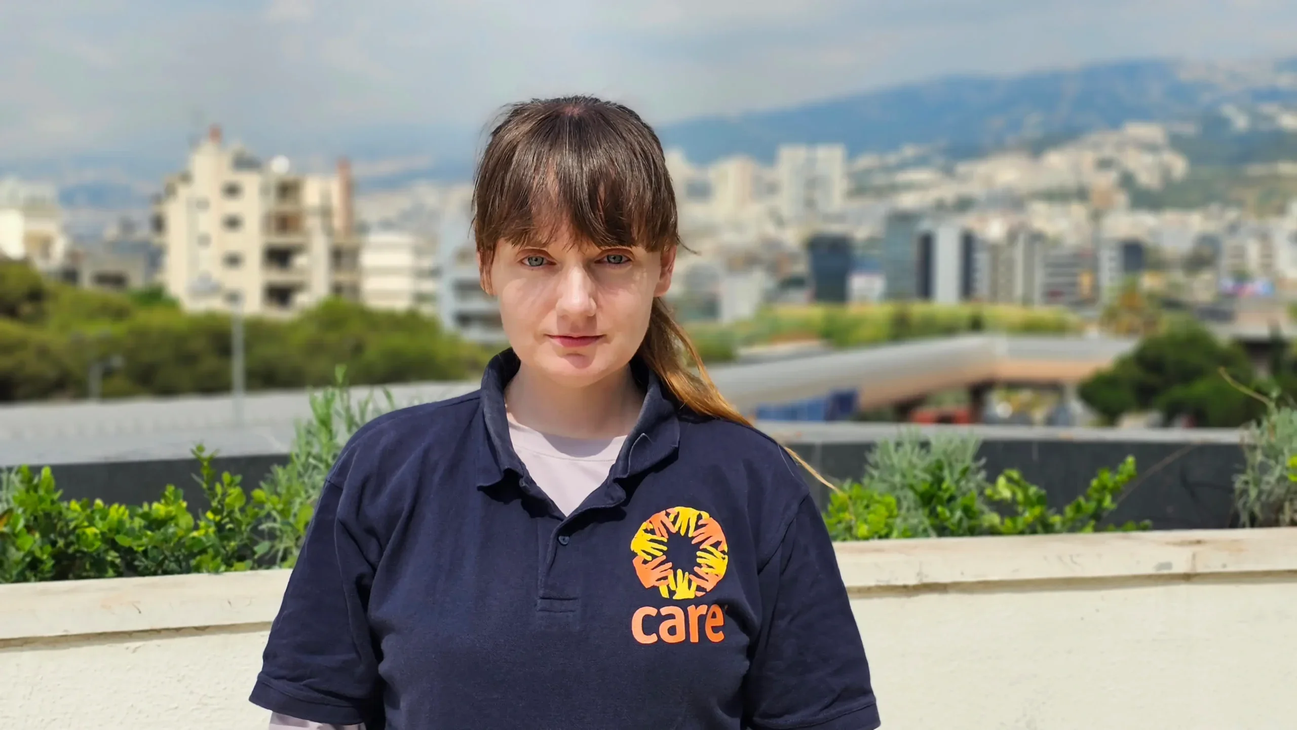 Woman aid worker in Lebanon looking into camera with city in background.