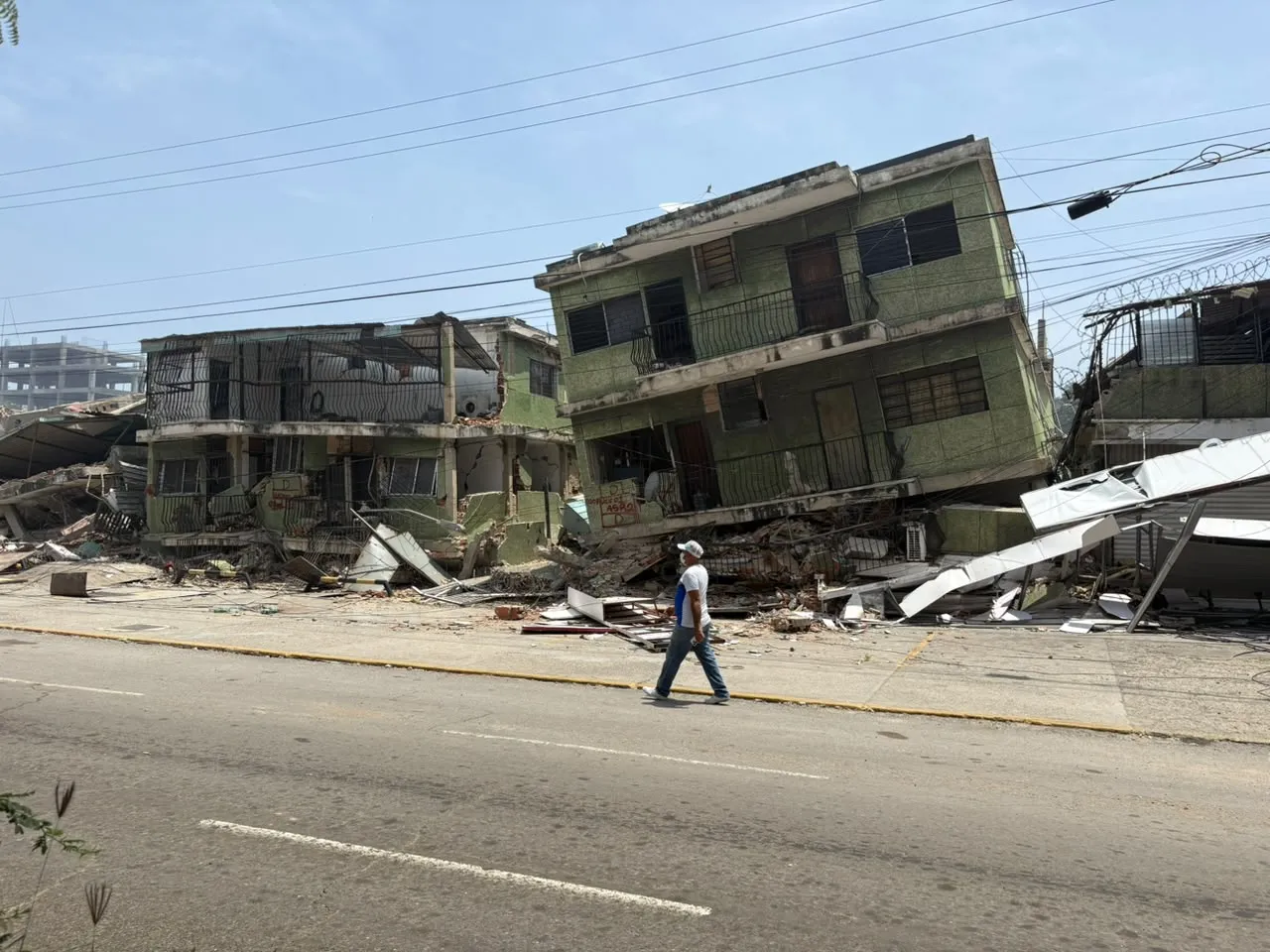 A person walking down an empty street in Venezuela with earthquake destruction in the background.