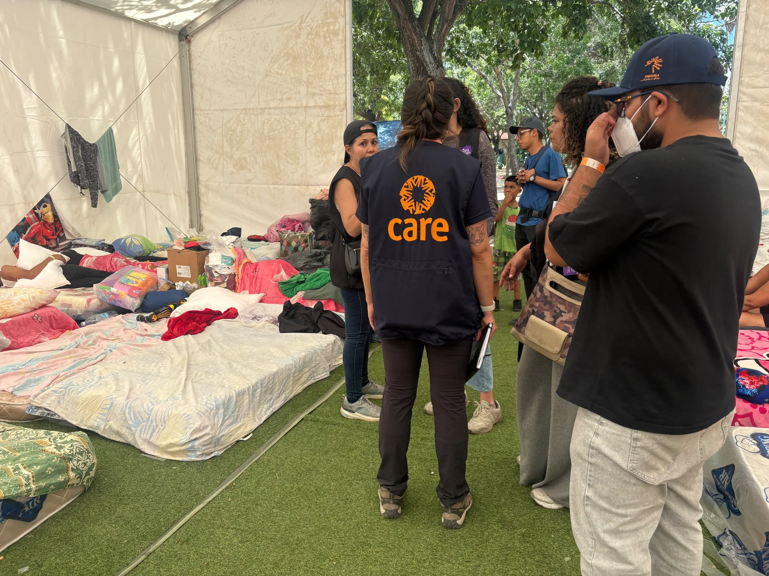 A group of aid workers gathered together inside a tent shelter with beds on the ground beside them.