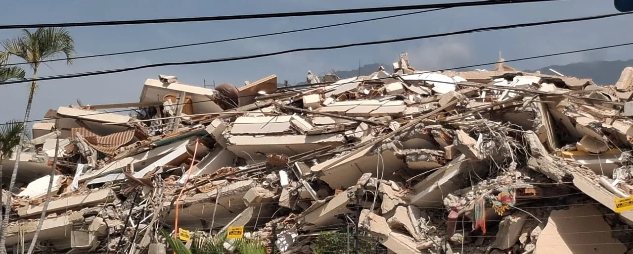 A massive, tangled pile of shattered concrete slabs, rebar, and debris from a completely collapsed building in La Guaira, Venezuela.