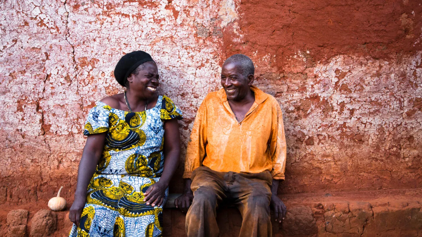 Two smiling people sit beside a wall in Zambia.