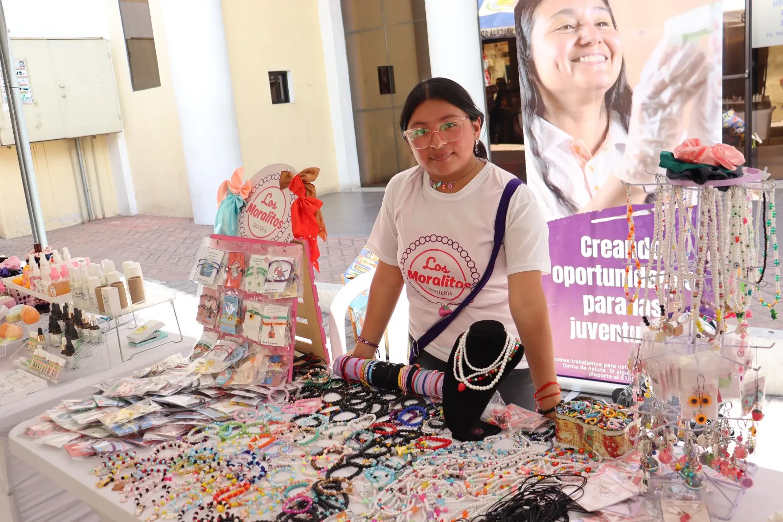 A young woman standing by a table of colorful jewelry she created.