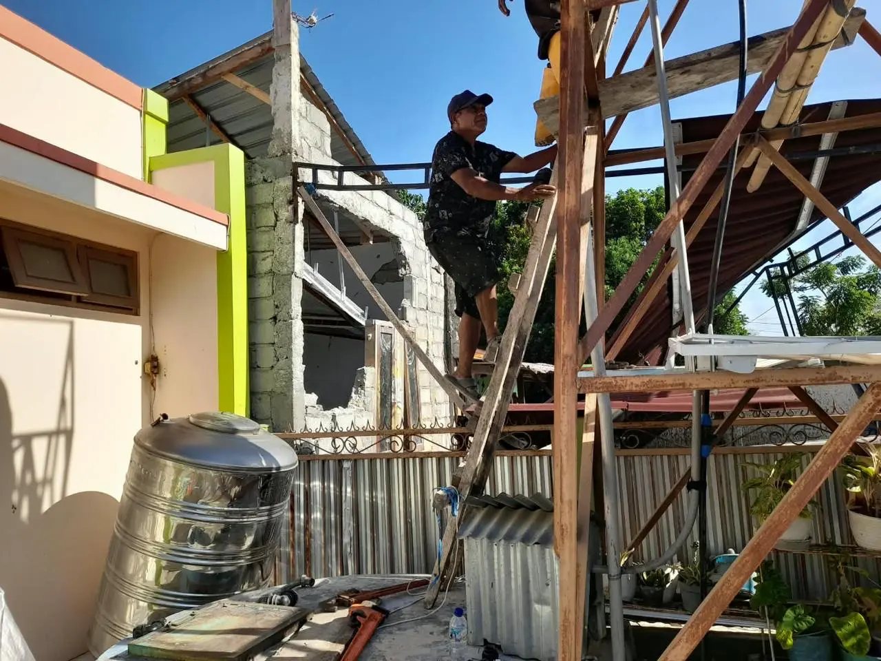 A man is standing on a ladder and inspecting damage to a building after the earthquake in Indonesia.